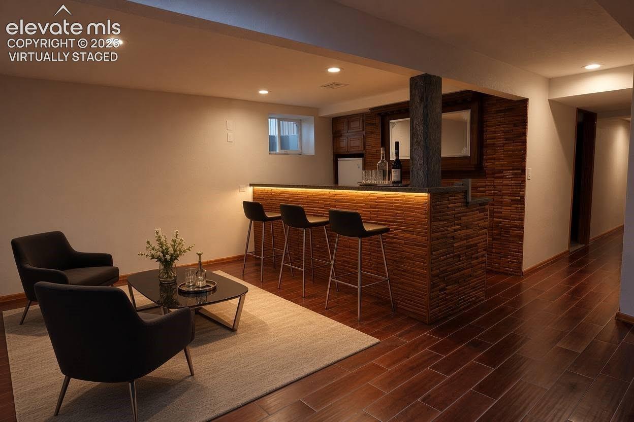 Built-in wet bar featuring stone-texture cladding, integrated under-counter lighting, recessed ceiling lighting, and wood-finish flooring, virtually staged 