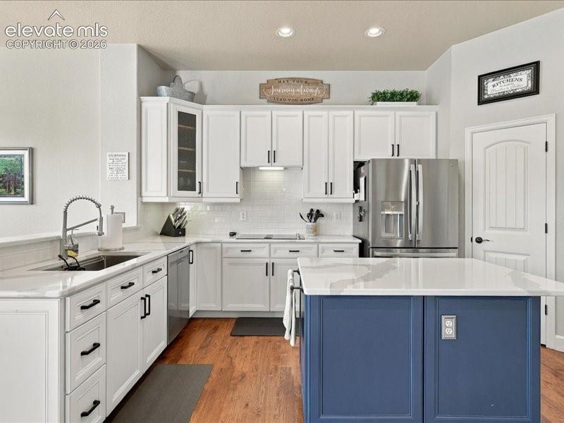 Kitchen featuring white shaker-style cabinetry, a blue island with a white countertop, stainless steel refrigerator, white subway tile backsplash, and wood-finish flooring
