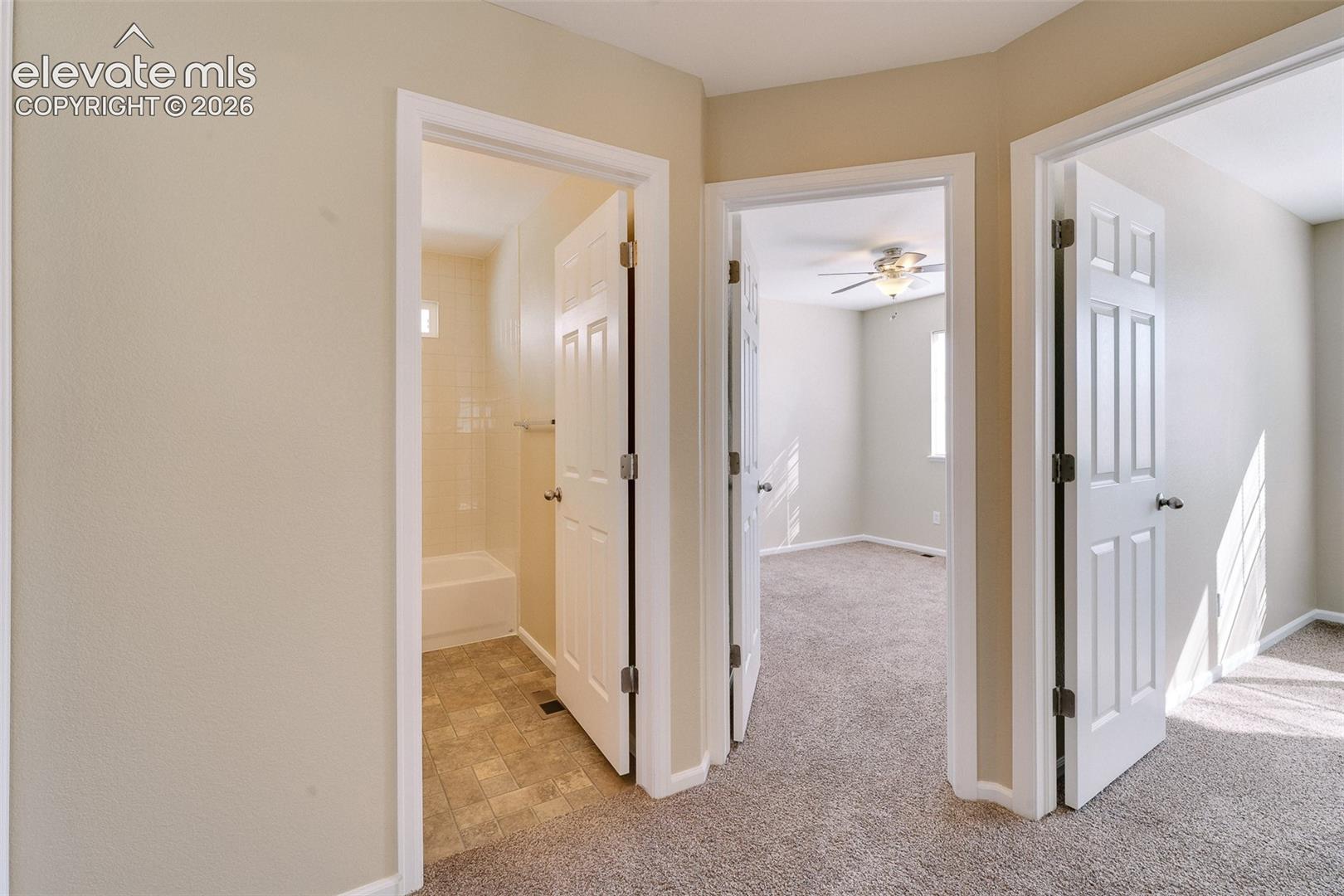 Neutral wall palette, six-panel interior doors, plush carpeting, tiled bathroom flooring, and ceiling fan fixture