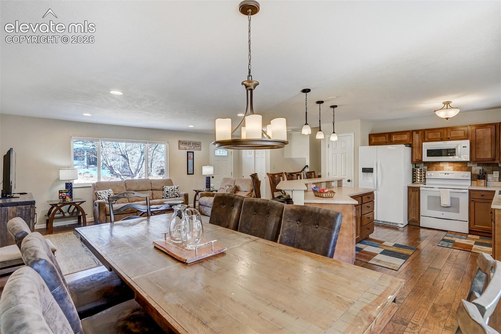 Open-concept living area with wood-finish flooring, recessed lighting, and a kitchen featuring wood cabinetry, white appliances, and a central island with pendant lighting