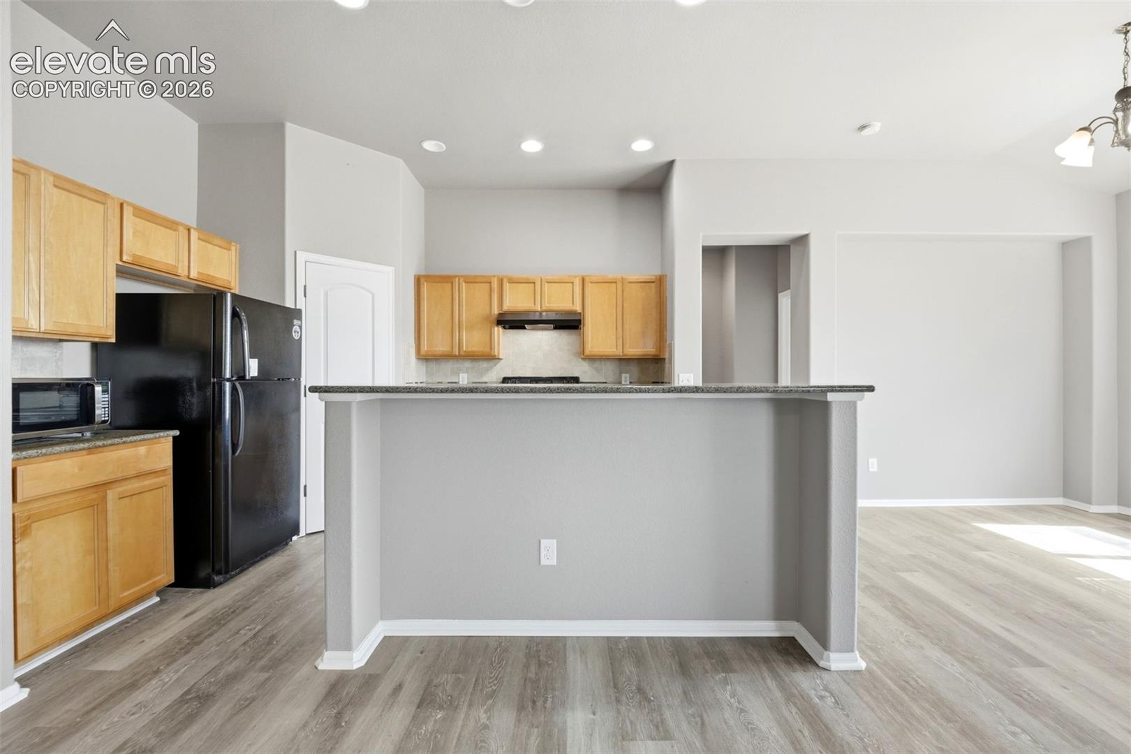 Kitchen featuring wood-finish cabinetry, black appliances, light-toned backsplash, and a breakfast bar with a dark countertop