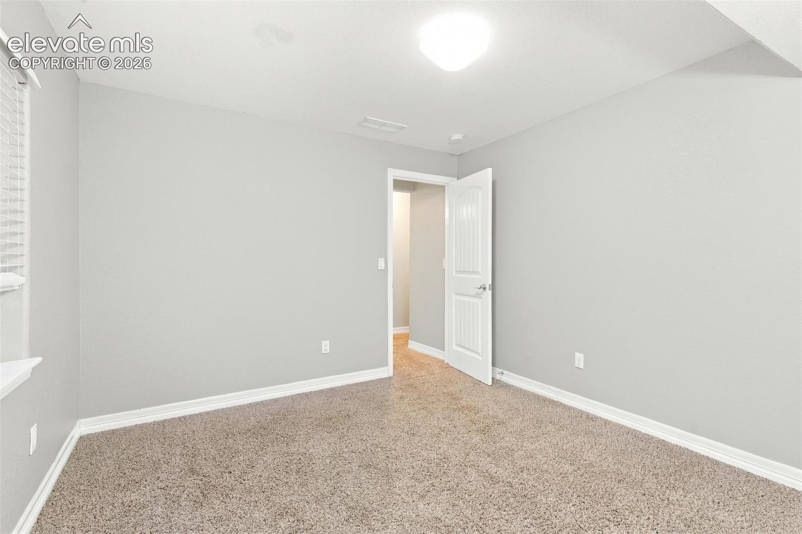 Room featuring neutral wall tones, wall-to-wall carpeting, a multi-panel interior door, and flush-mount ceiling lighting