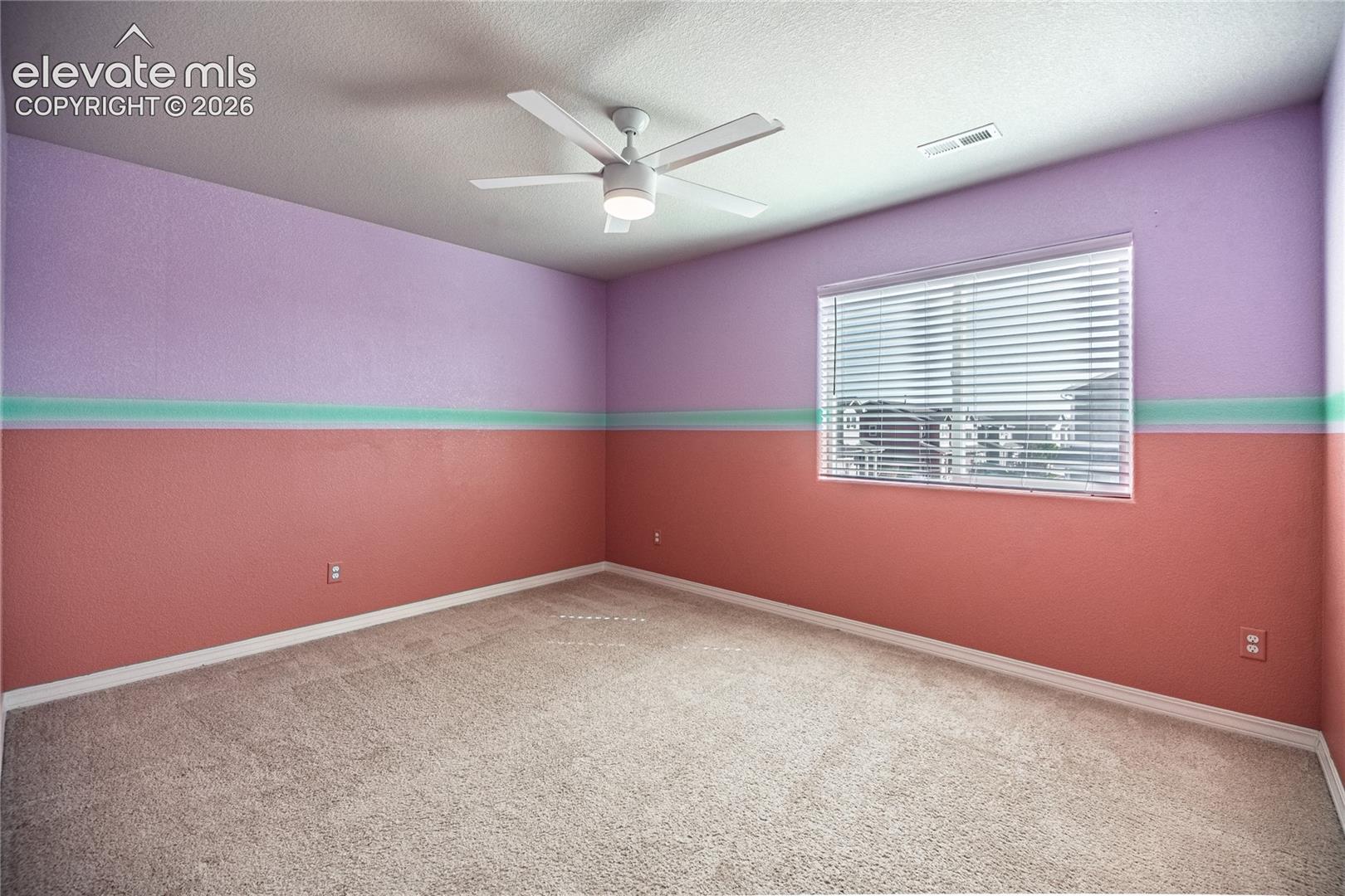 Textured walls with a two-tone paint scheme, a single window with blinds, and a ceiling fan with integrated lighting