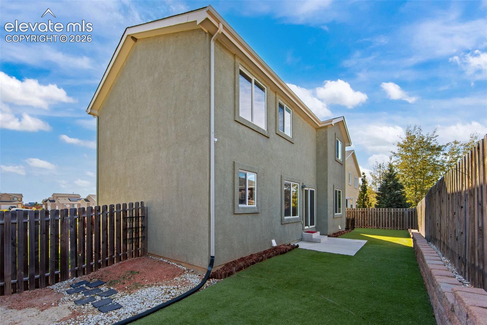 Stucco exterior, fenced backyard with artificial turf, concrete patio, and segmented masonry retaining wall
