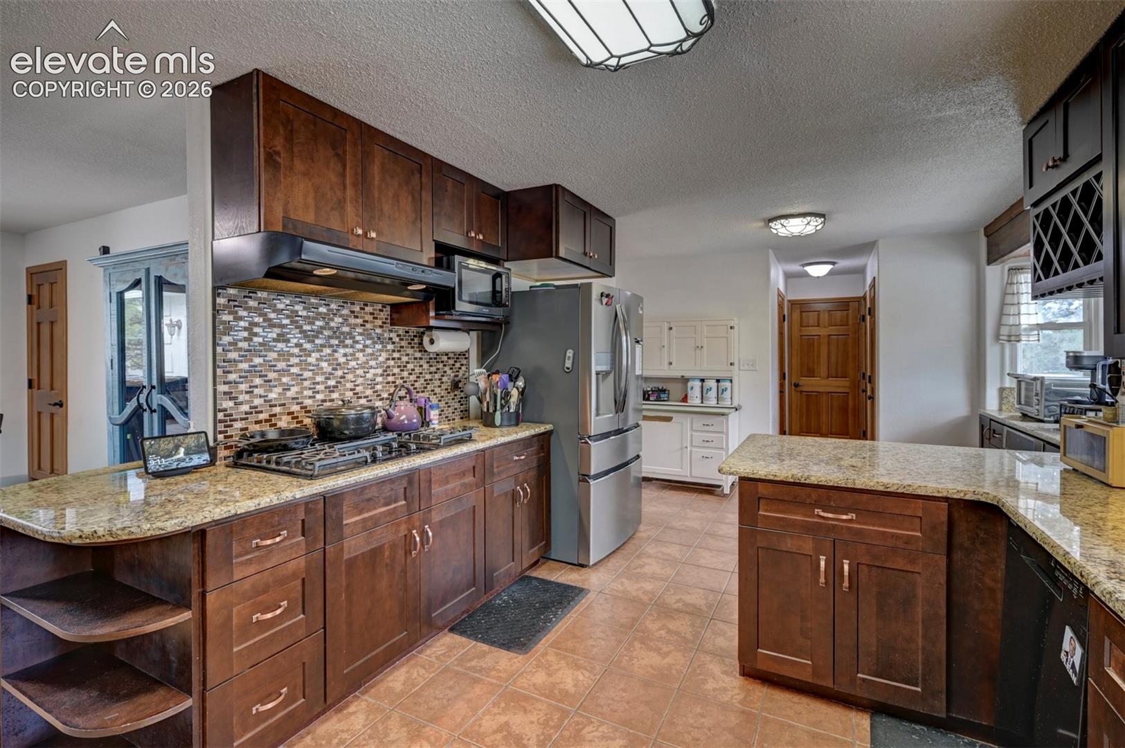 Kitchen featuring dark wood-finish cabinetry, light speckled countertops, a mosaic tile backsplash, and tile flooring