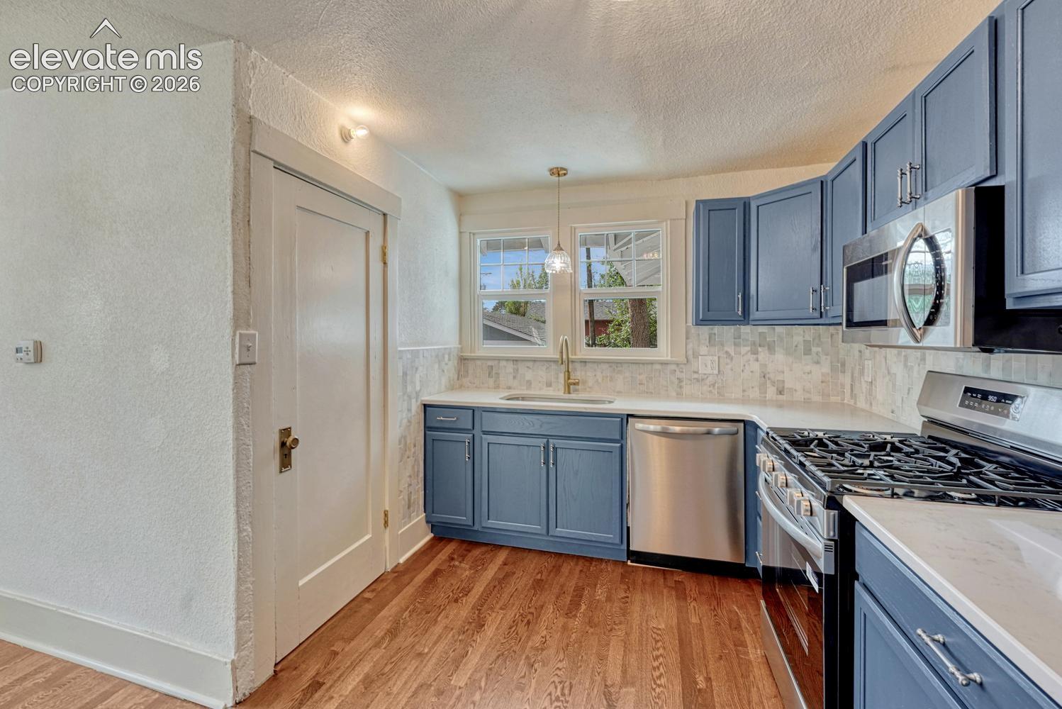 Kitchen featuring blue cabinetry, white countertops, stainless steel appliances, wood-finish flooring, and a tiled backsplash