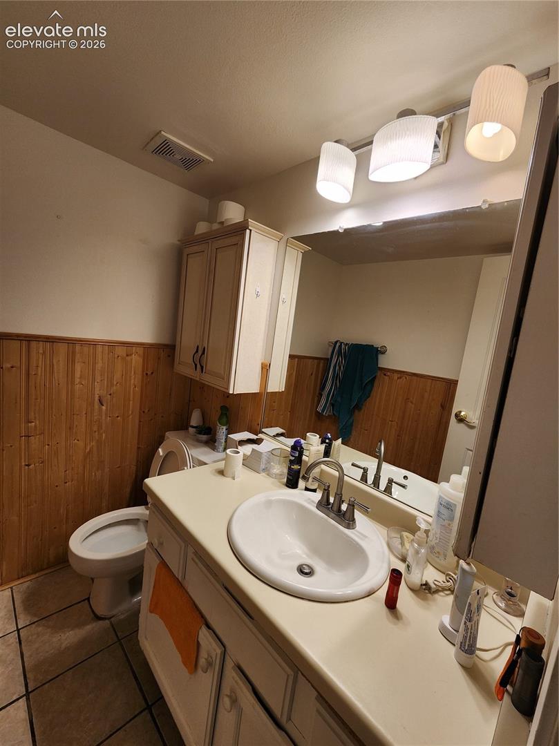 Vanity featuring a solid-surface countertop with an integrated oval sink, paired with a three-light fixture, wood wainscoting, and ceramic tile flooring