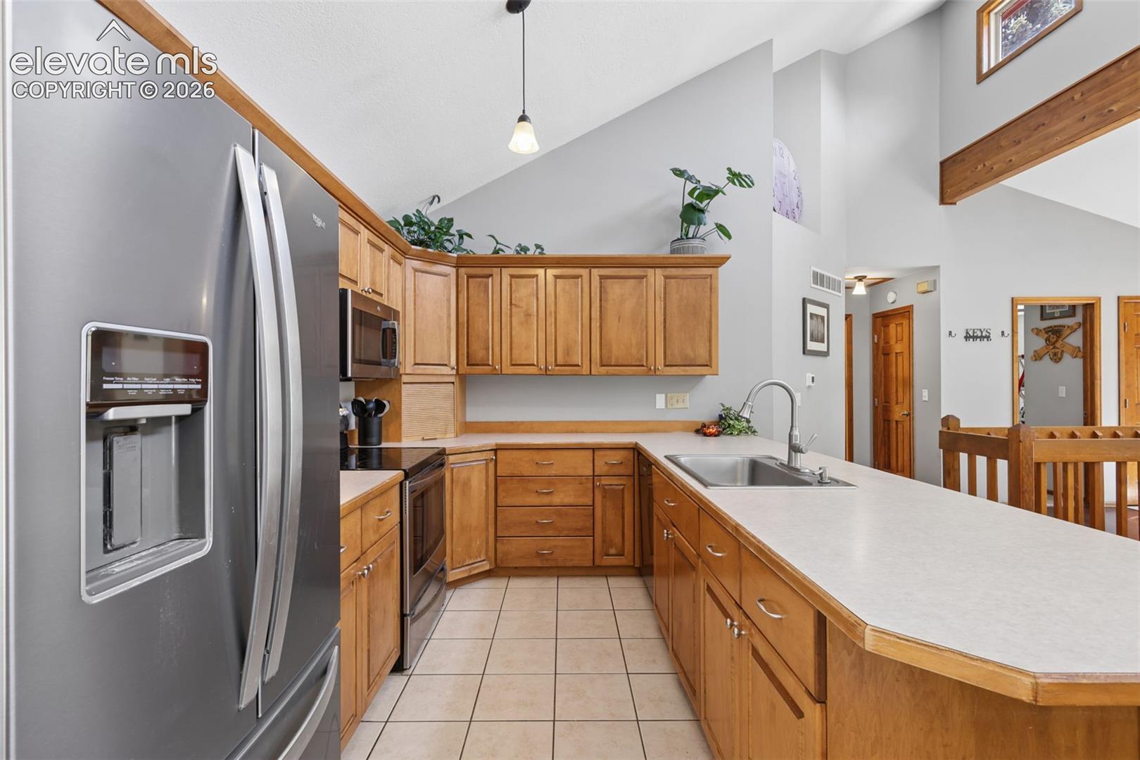 Kitchen featuring wood cabinetry, stainless steel appliances, a double basin sink, and tile flooring