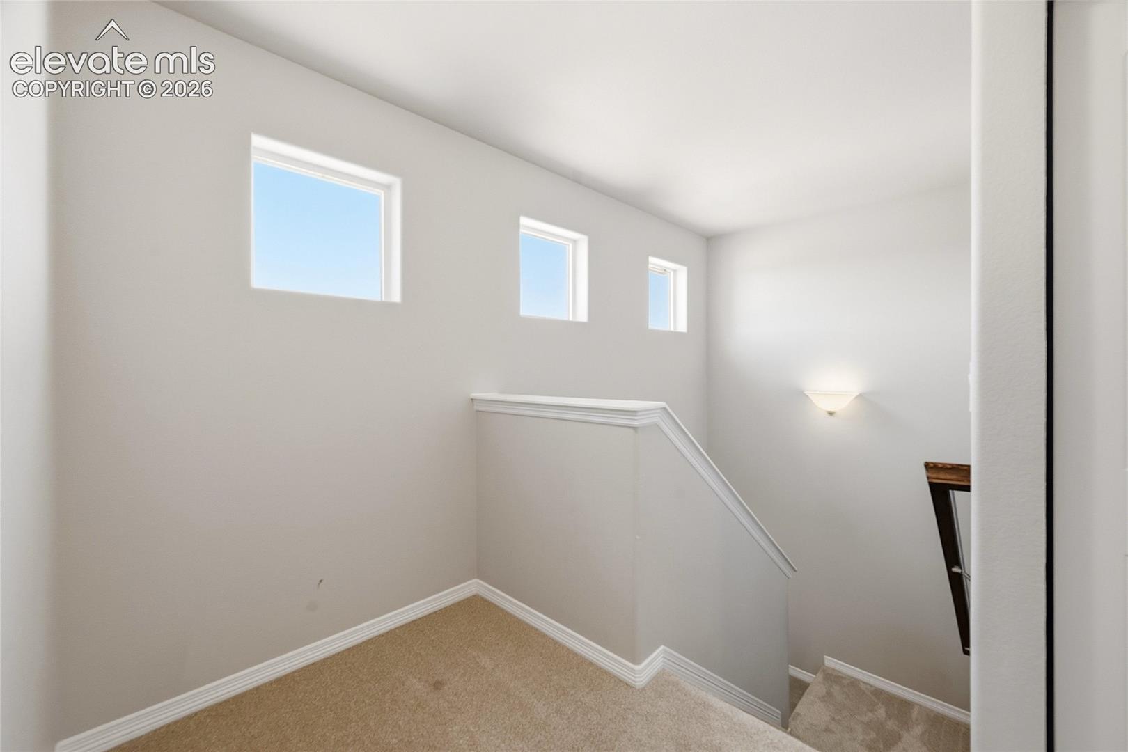 Upper-level landing featuring three rectangular windows, neutral wall tones, and carpet flooring