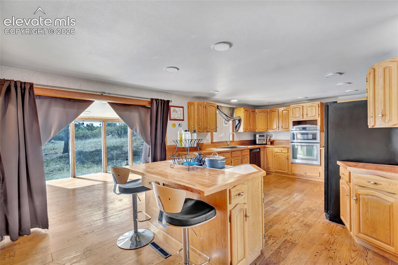 Kitchen featuring wood-finish flooring, wood cabinetry, a center island with countertop seating, and double wall ovens