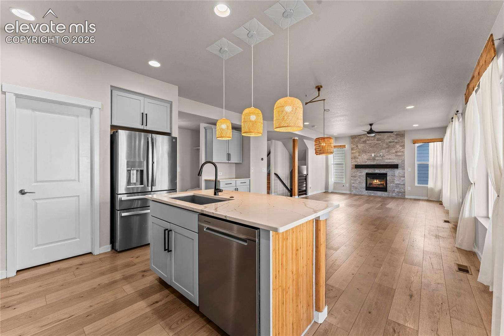 Kitchen island with stone-finish countertop, stainless steel appliances, wood-finish flooring, and floor-to-ceiling stone fireplace