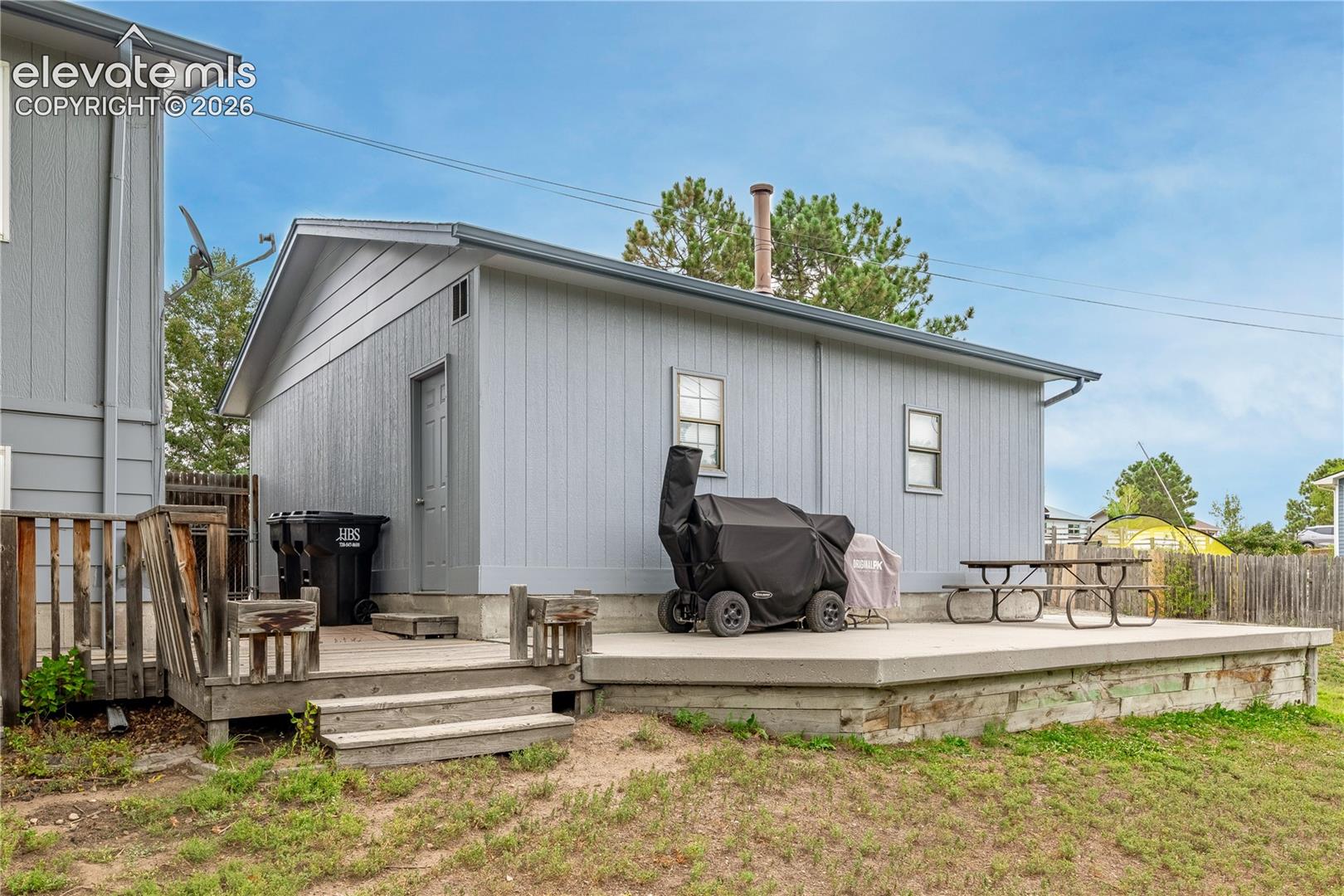 Detached structure featuring vertical siding, a concrete patio, and a tiered wood deck