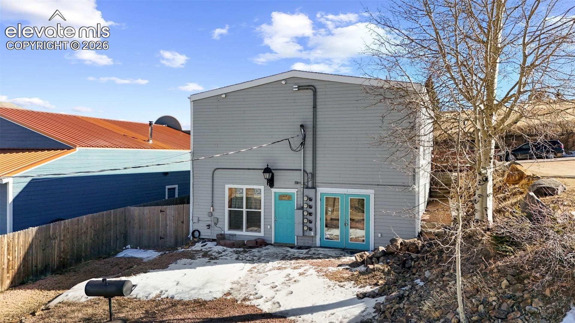 Gray horizontal siding exterior featuring dual glass-panel entry doors, a single-hung window with white trim, and wall-mounted exterior lighting