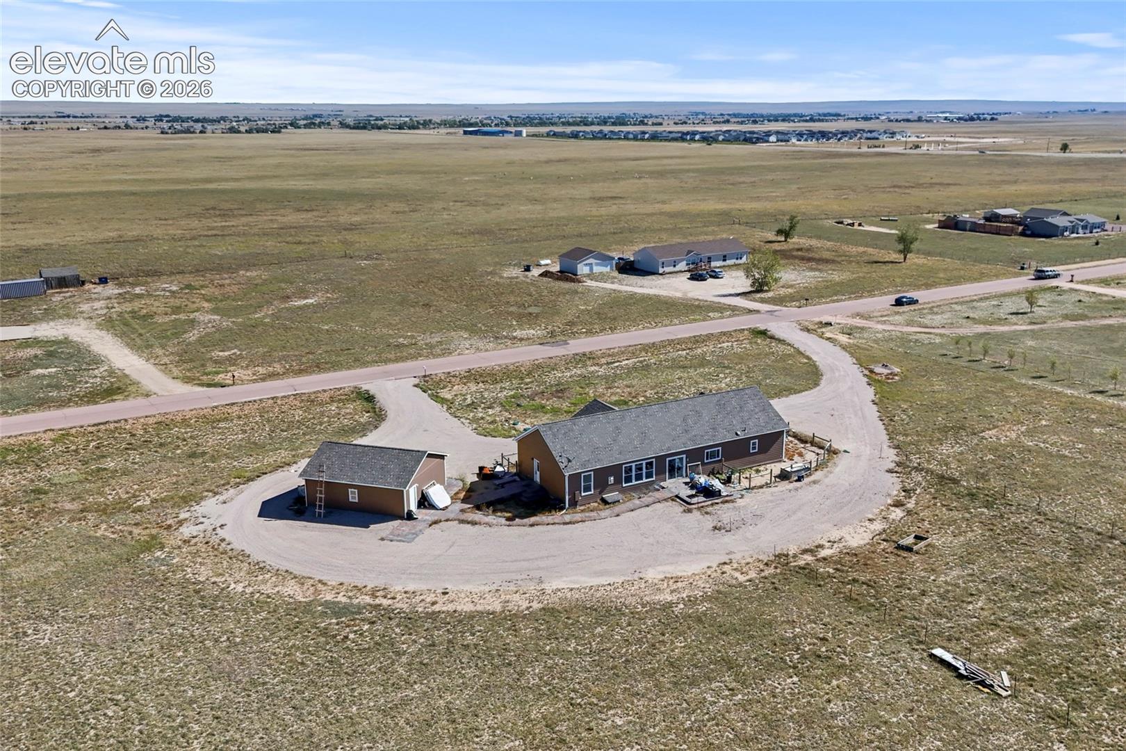 Expansive property featuring a single-story residence, a detached garage, and a wrap-around gravel driveway on a vast acreage lot