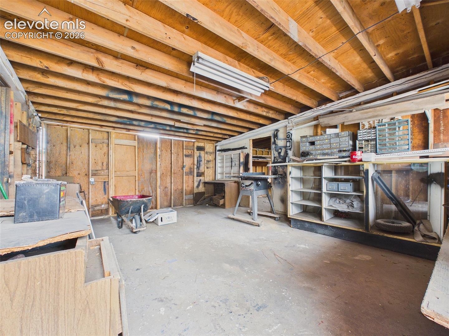 Versatile workshop space featuring exposed ceiling beams, concrete flooring, built-in shelving, work surfaces, and organized storage compartments.