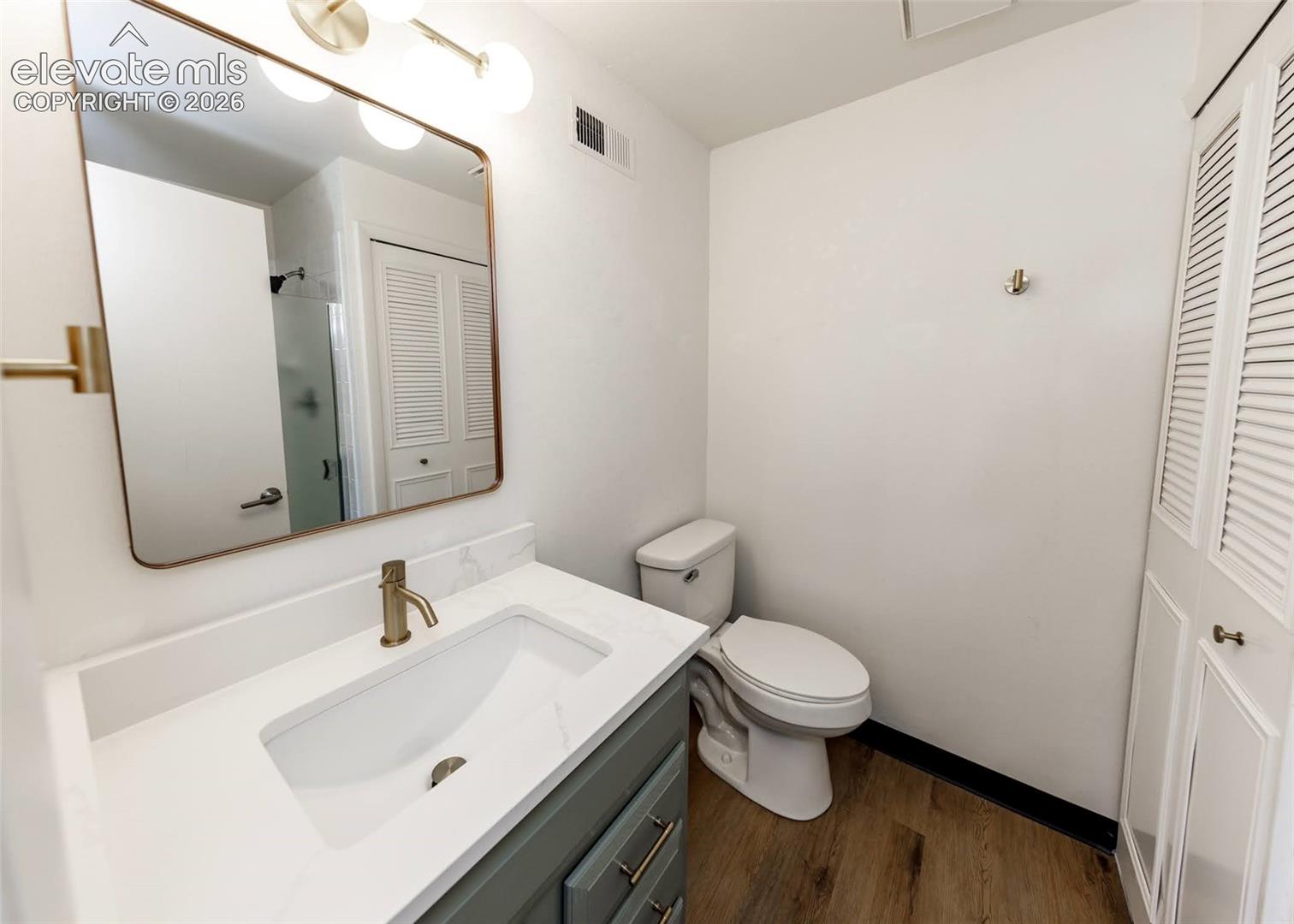 Single vanity with white countertop, integrated rectangular sink, metallic faucet, gold-rimmed mirror, and louvered-panel cabinetry