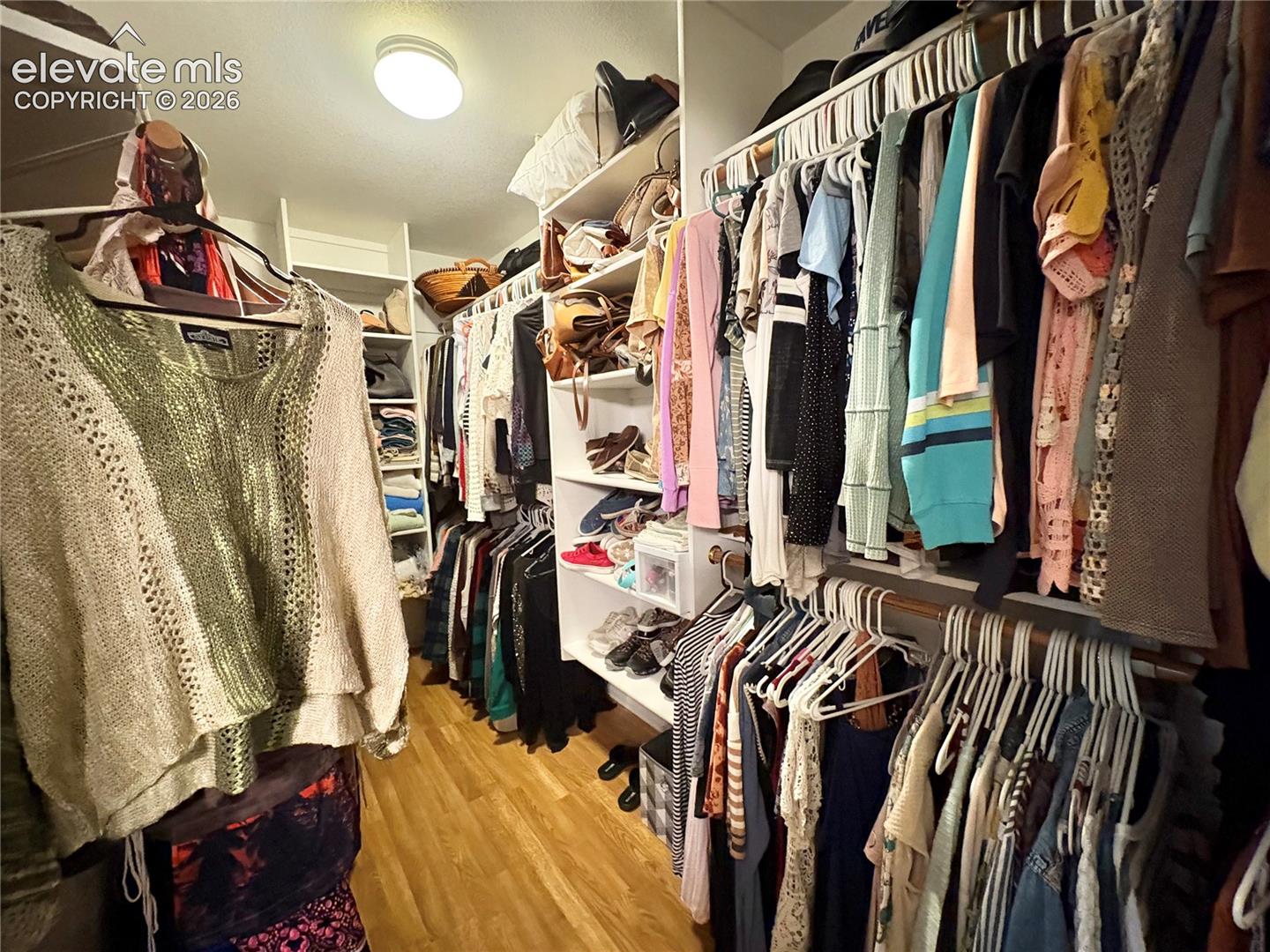 Walk-in closet featuring wood-finish flooring, built-in shelving, and ample hanging rod space