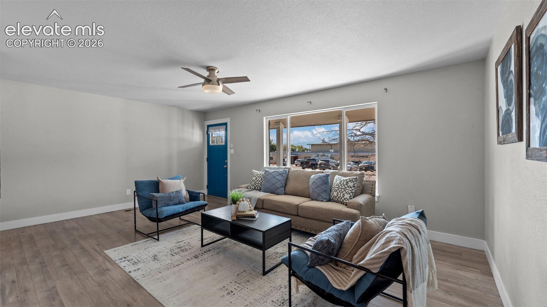Spacious living area featuring wood-finish flooring, a ceiling fan, and ample natural light from a large front-facing window