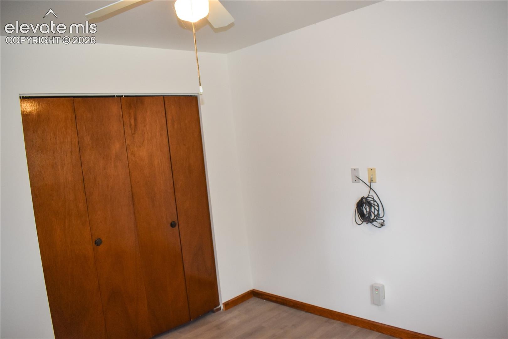 White walls with a ceiling fan light fixture, wood-finish flooring, and wood baseboards
