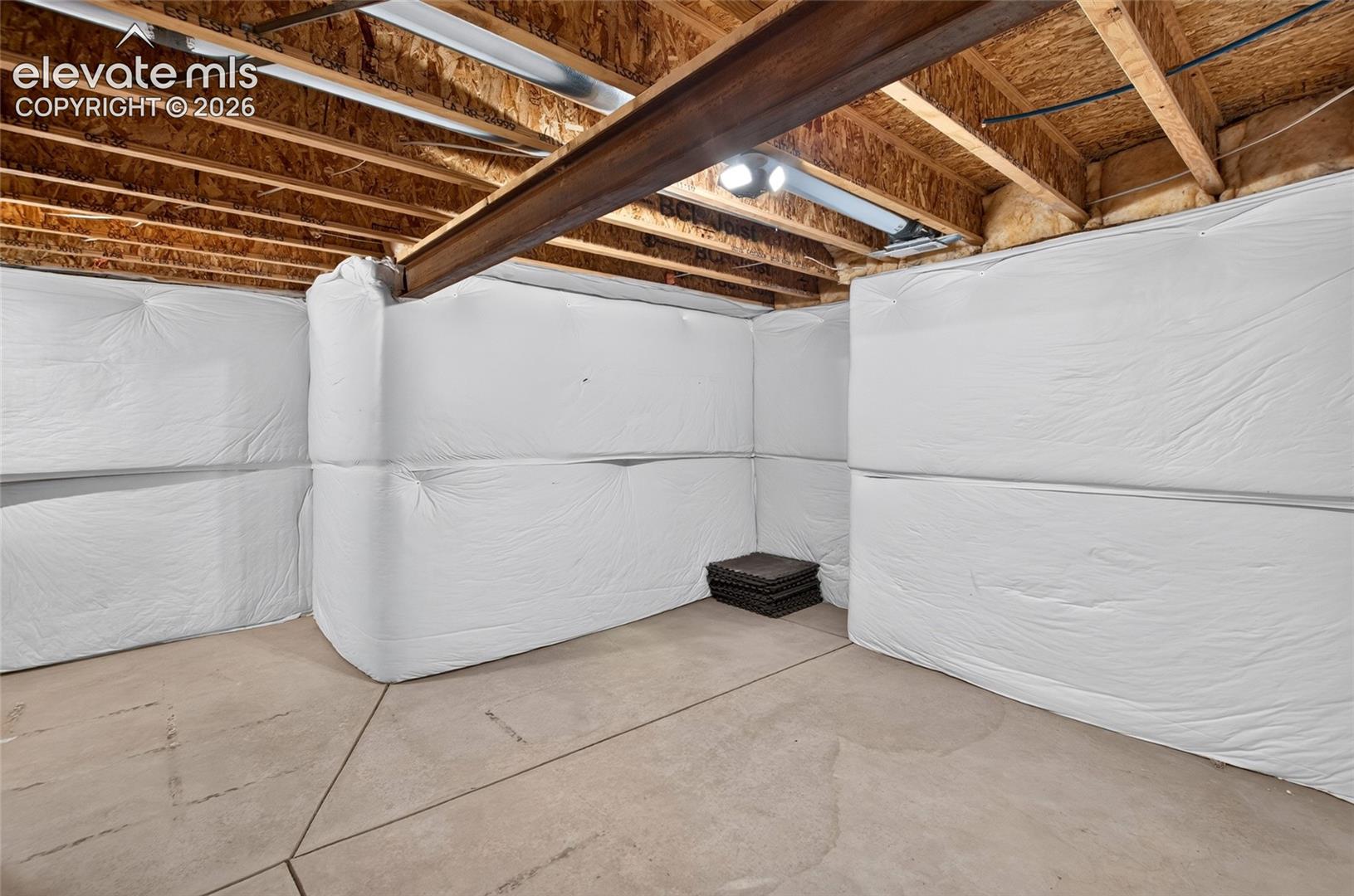Unfinished basement featuring exposed wood joists and a steel support beam insulated storage area