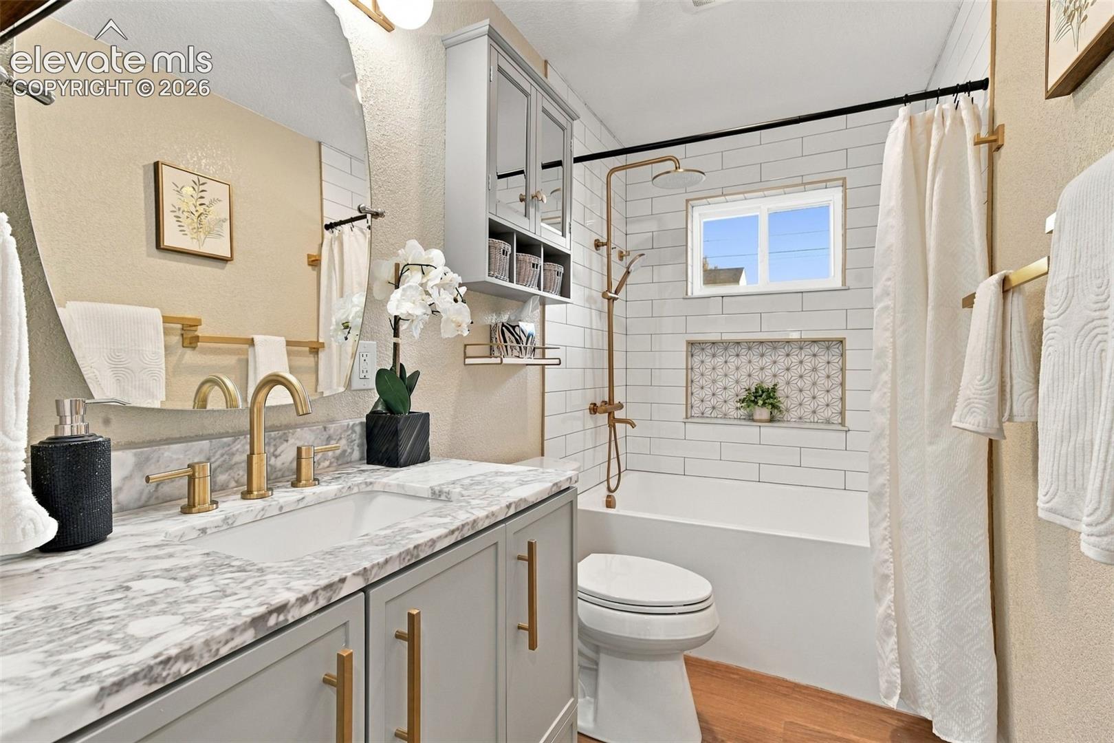 Bathroom featuring a stone-surface vanity with gold-tone fixtures, wall-mounted storage cabinetry, a recessed shower niche, and white subway tile wall surrounds