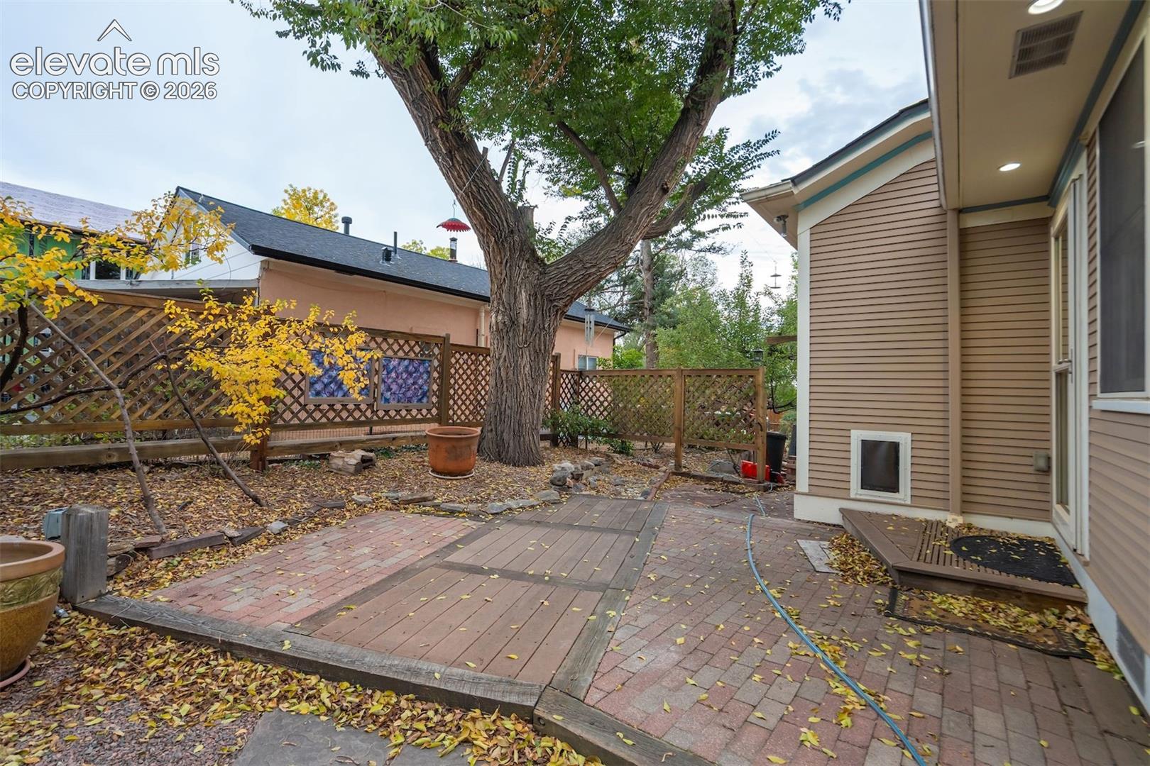 Paved patio area with brick and wood-finish sections, bordered by a wooden lattice fence