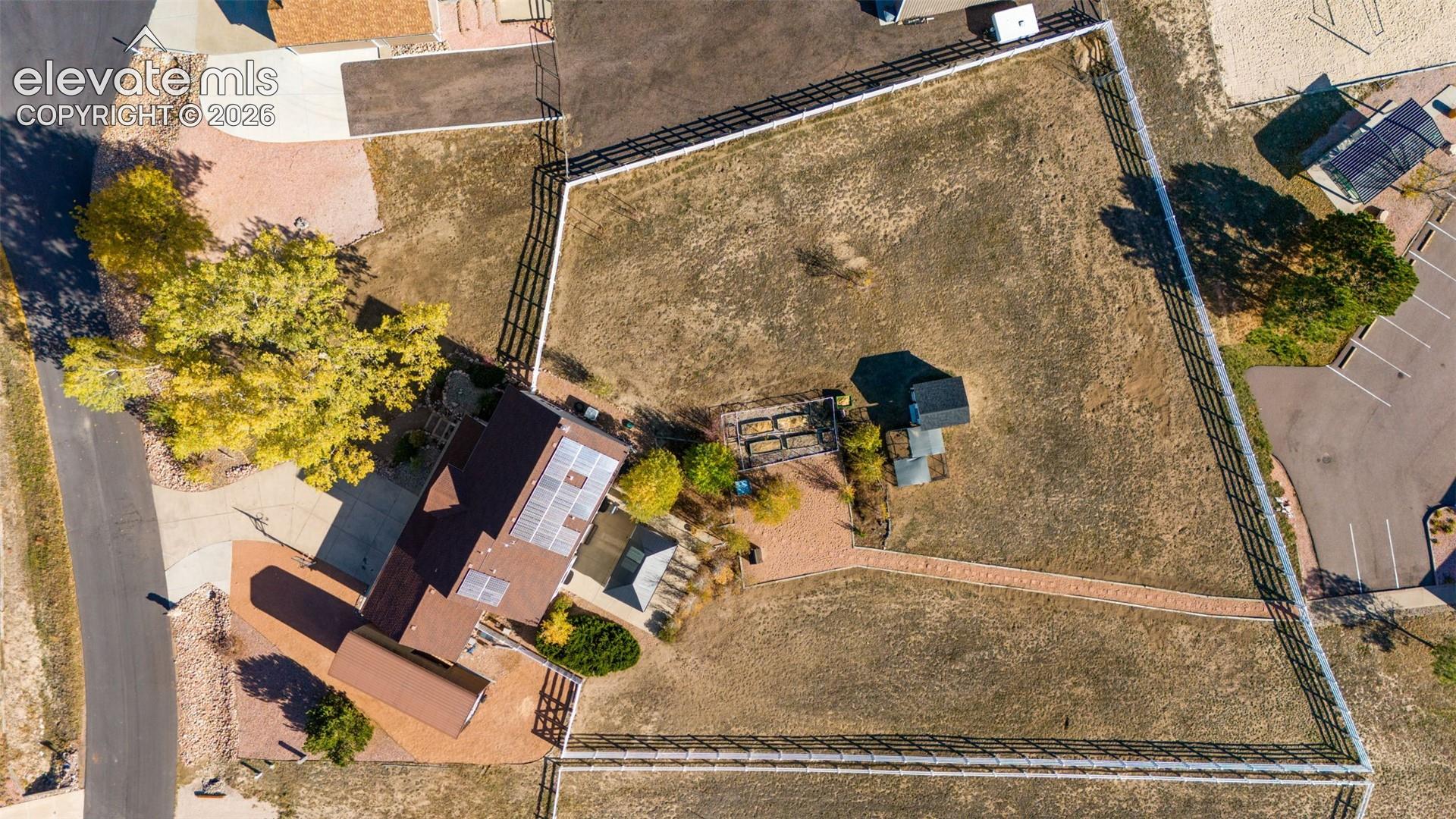 Aerial perspective of a property featuring solar panels, a fenced-in perimeter, a paved walkway, and raised garden beds