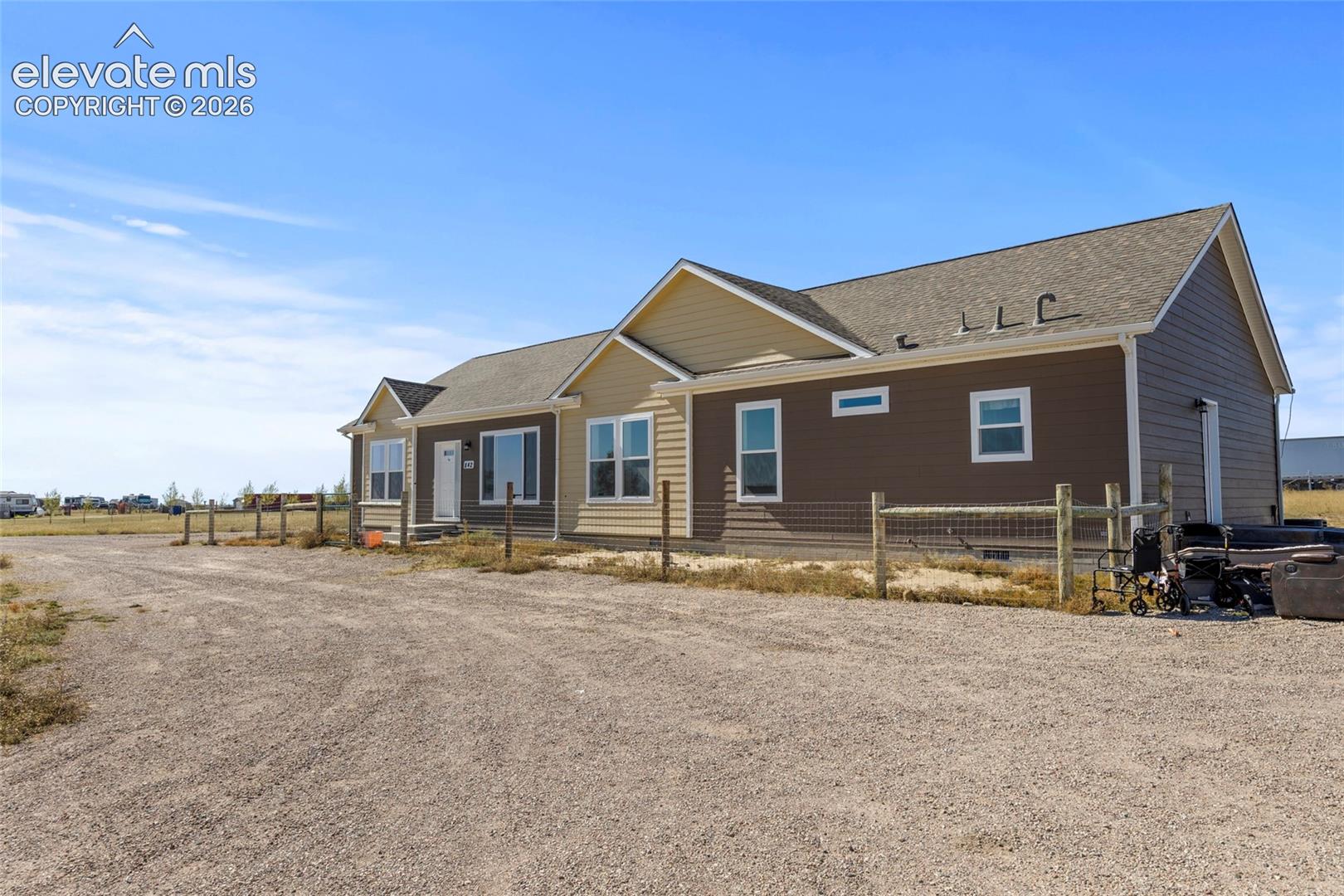 Single-story exterior featuring multi-toned horizontal lap siding, a pitched roof, and a gravel driveway bordered by post-and-wire fencing