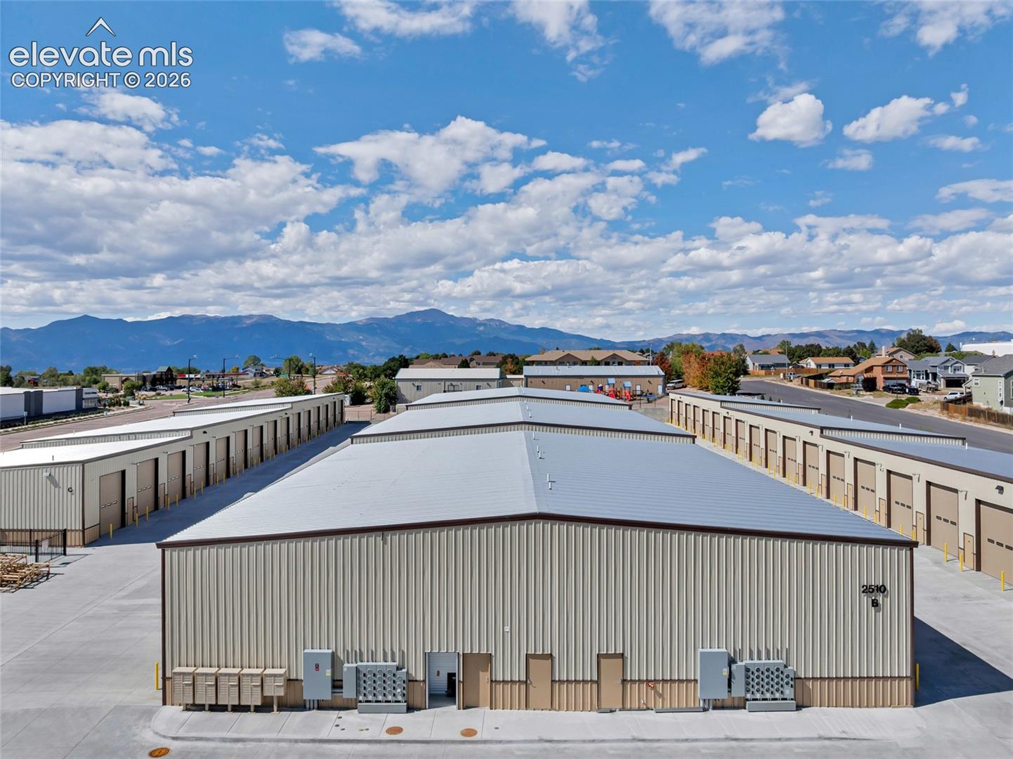 Metal-sided storage facilities with multiple unit doors, concrete driveways, and a distant mountain backdrop