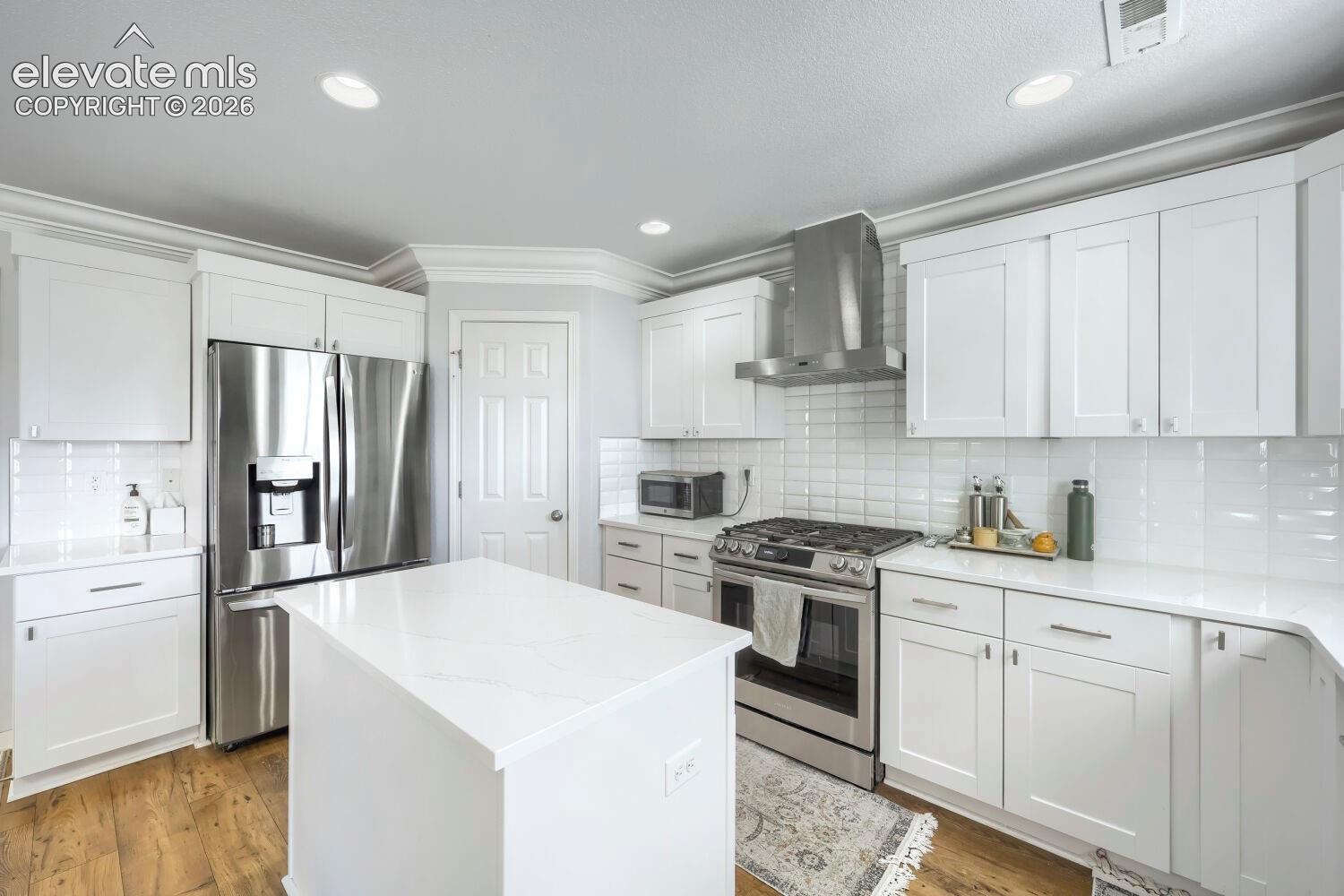 Kitchen featuring white shaker-style cabinetry, quartz countertops, a central island, stainless steel appliances, and subway tile backsplash