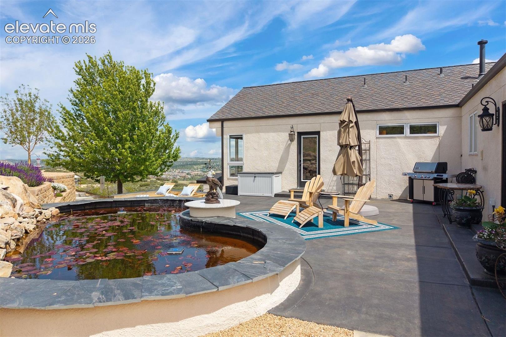 The sprawling patio anchors a backyard complete with a white sand beach seating area, lili pad water feature, lush flower gardens, flagstone pathways, and lilac-lined hillside retreats. 