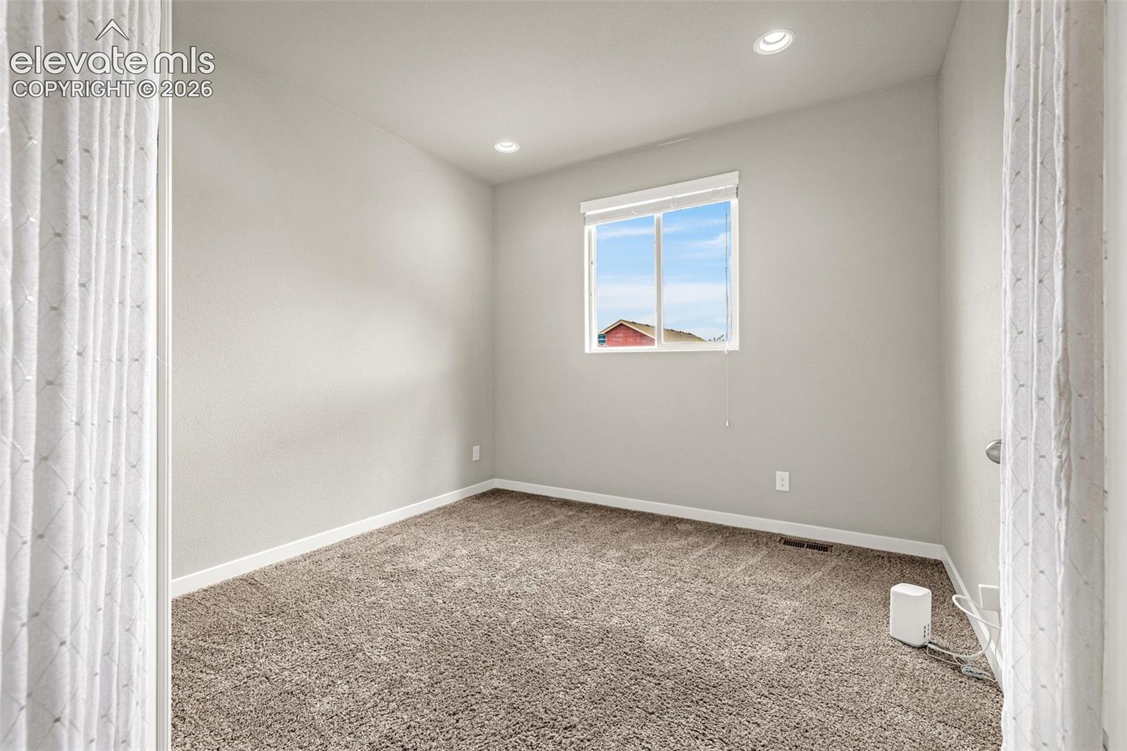 Neutral wall paint, recessed ceiling lighting, light-filtering window shade, and carpet flooring