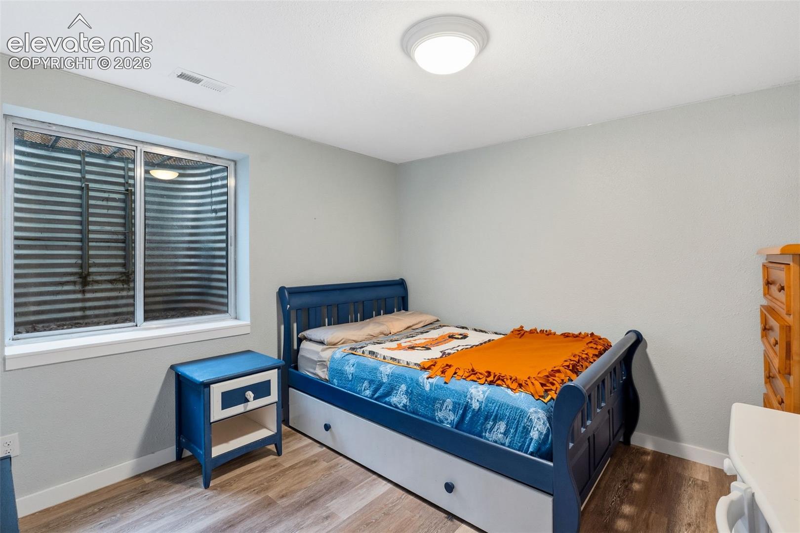 Recessed window with metal window well, wood-finish flooring, and overhead lighting