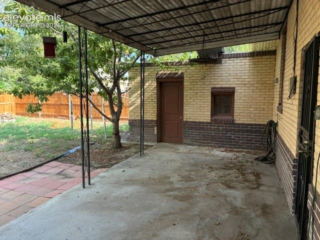 Concrete patio with a corrugated metal awning, bordered by a light-colored brick wall with a darker brick wainscot