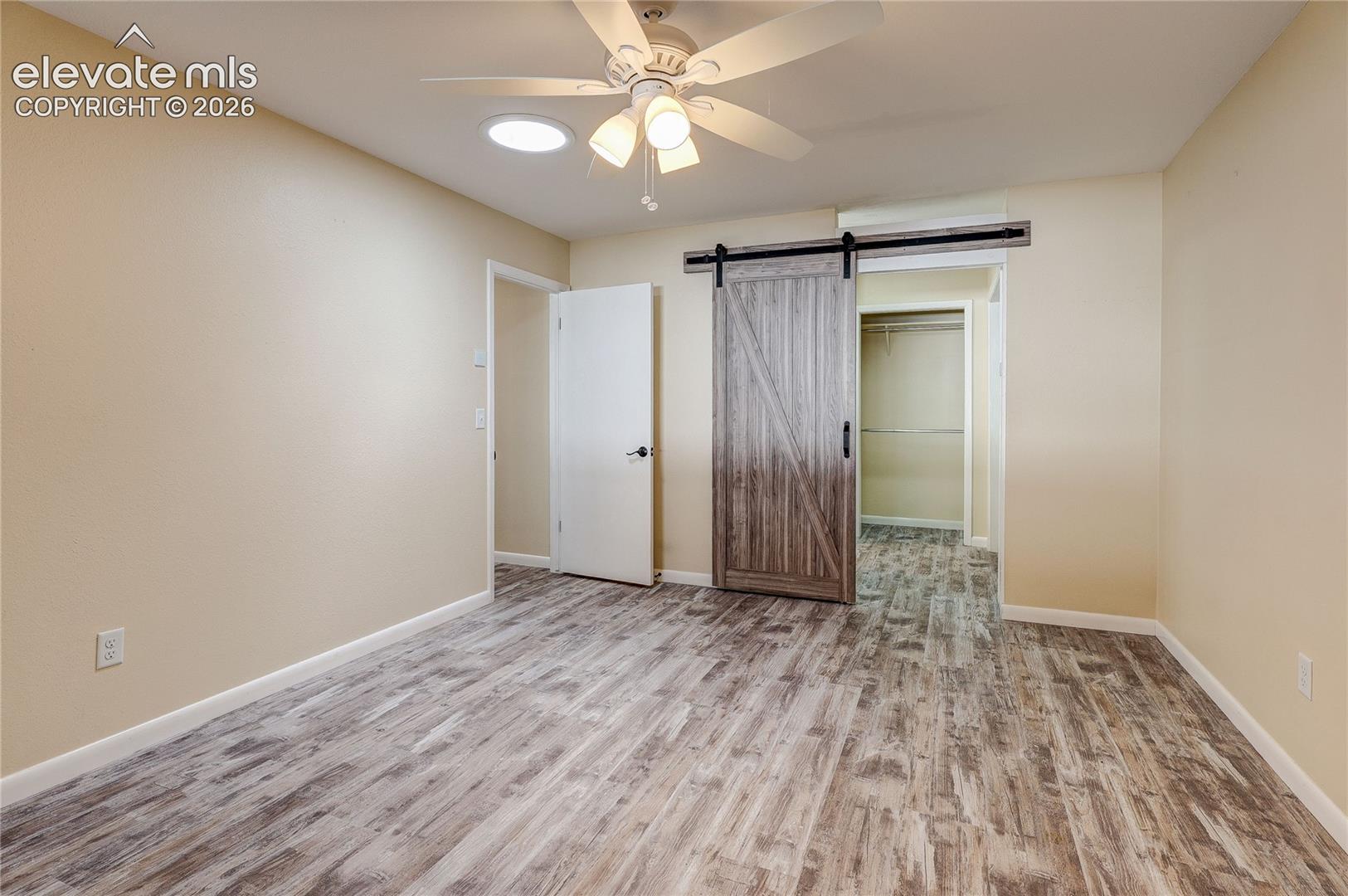 Interior room featuring wood-finish flooring, a ceiling fan with integrated lighting, a tubular skylight, and a sliding barn door entry
