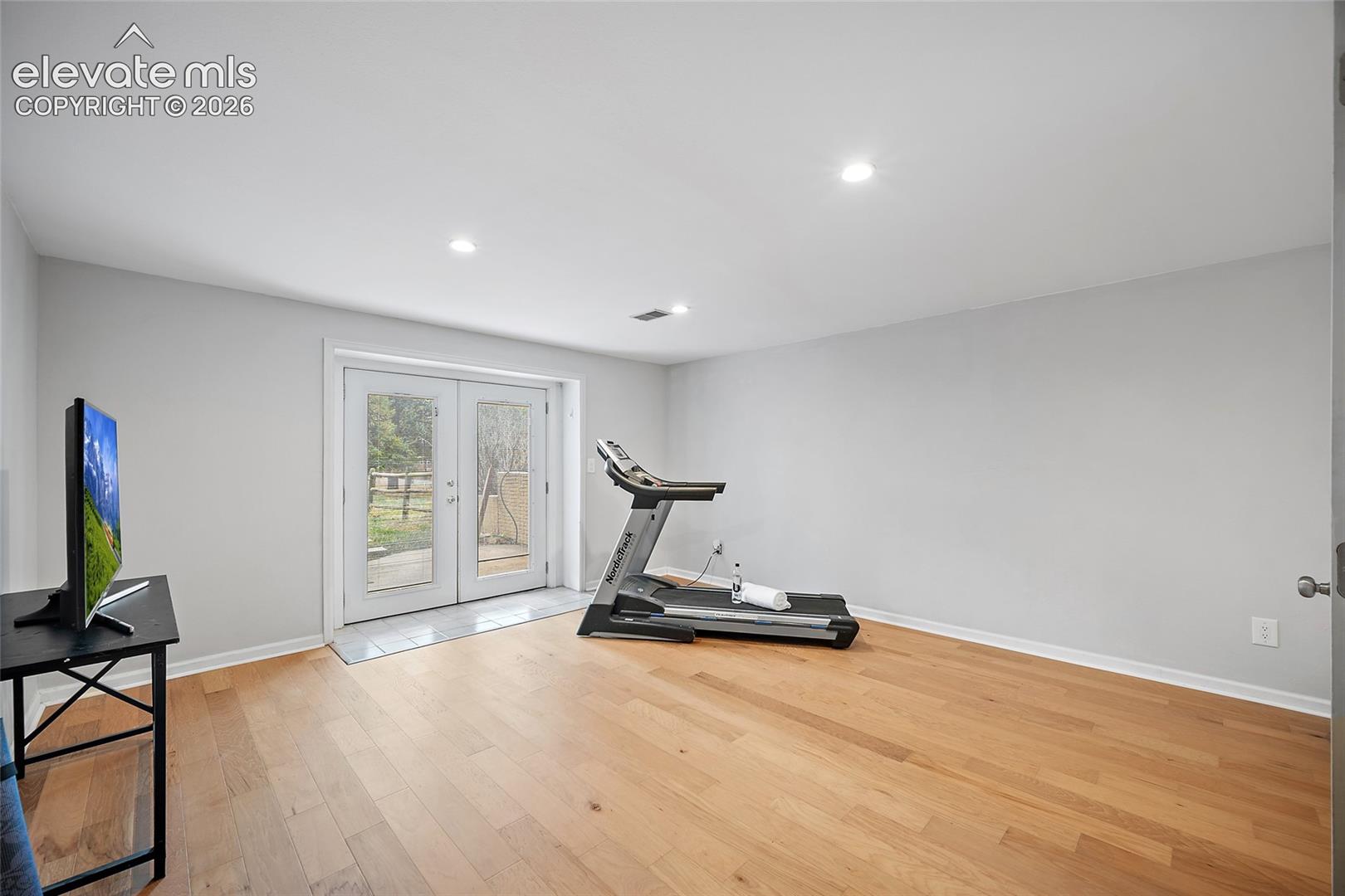 Neutral-toned interior featuring wood-finish flooring, recessed lighting, and double-glass paneled doors leading to an exterior paved surface