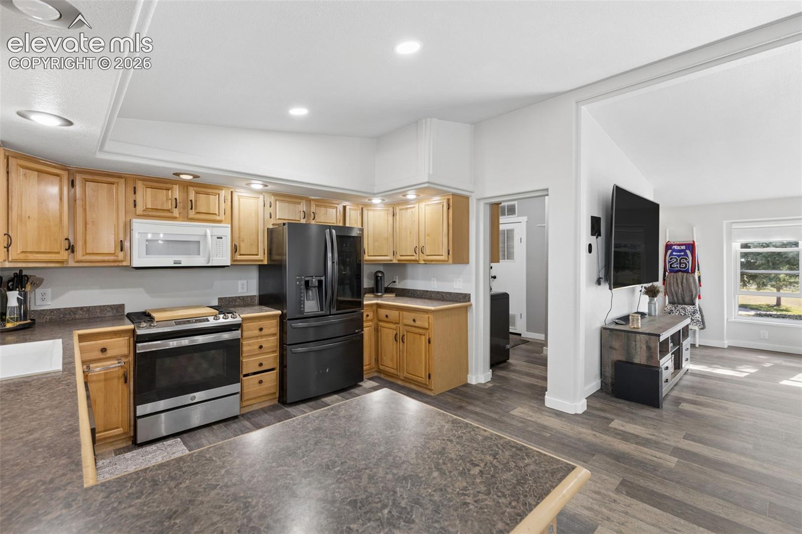 Kitchen featuring light-finish cabinetry, dark solid-surface countertops, stainless steel appliances, recessed ceiling lighting, and wood-finish flooring