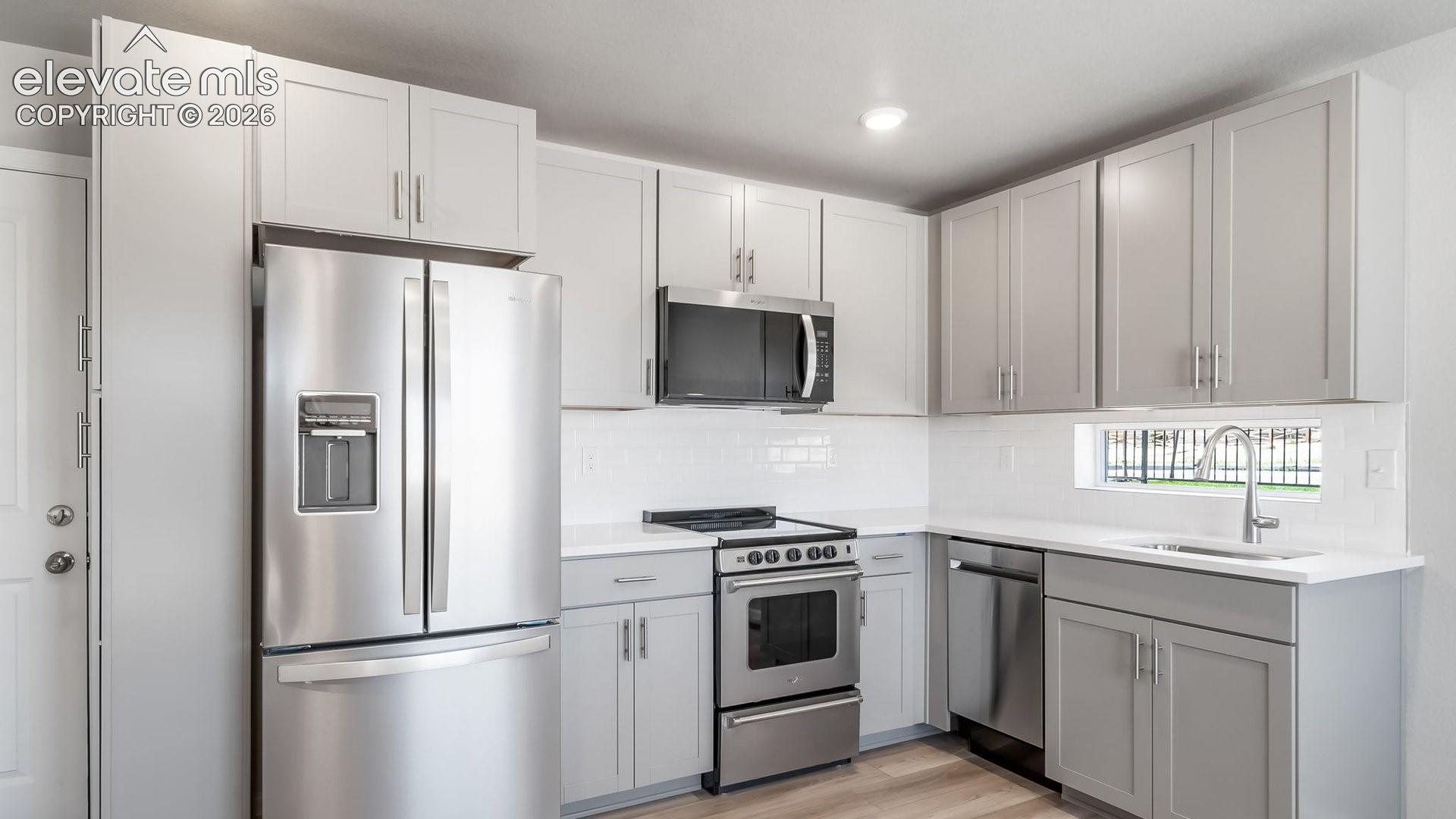 Kitchen featuring light grey Shaker-style cabinetry, white countertops, stainless steel appliances, a white tile backsplash, and wood-finish flooring
*photos of a model home*
