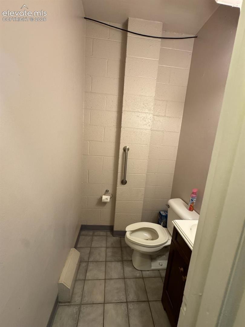 Tile flooring, wall-mounted grab bar, and a compact vanity with an integrated sink