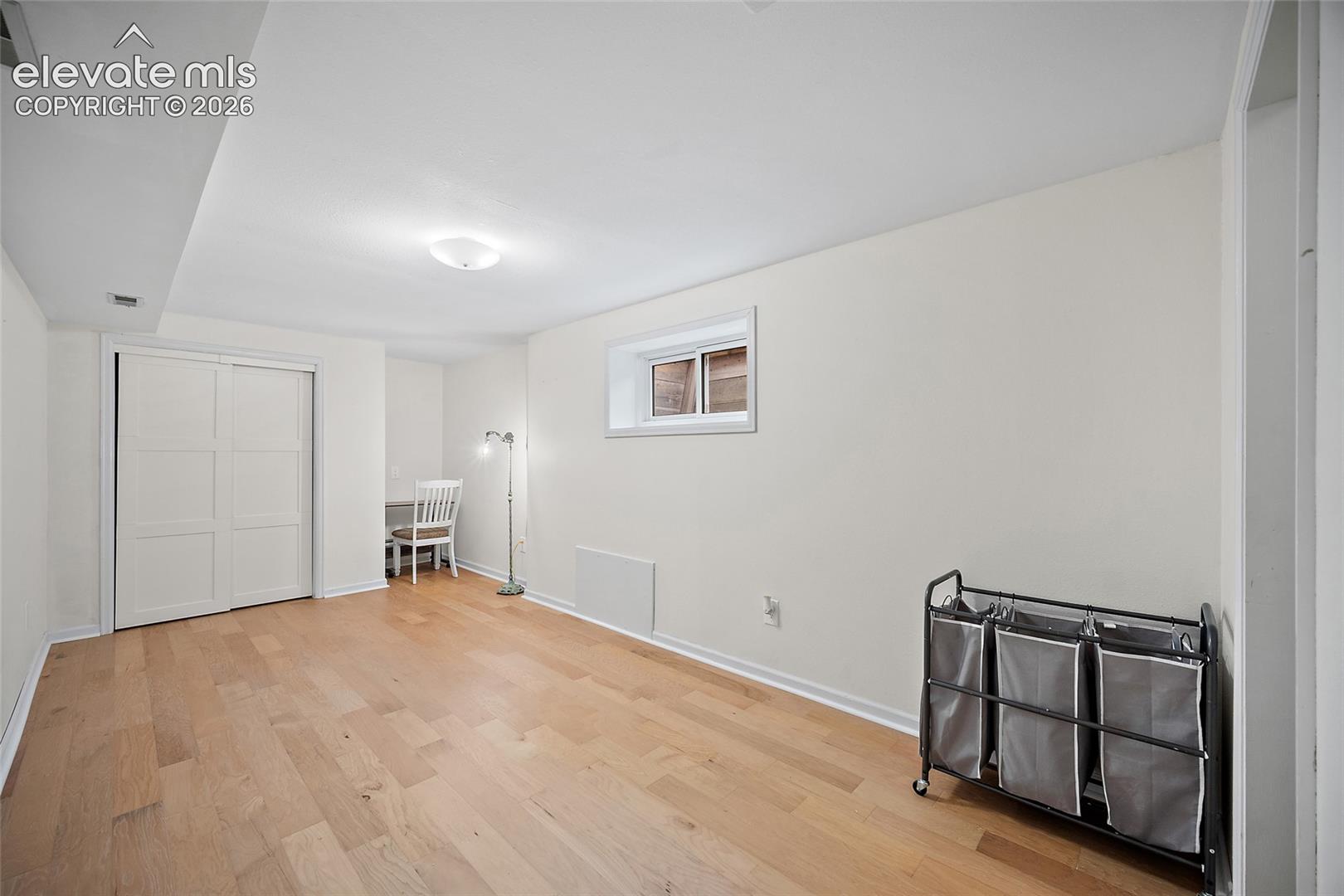 Room featuring wood-finish flooring, white walls, a built-in sliding door closet, and a recessed window