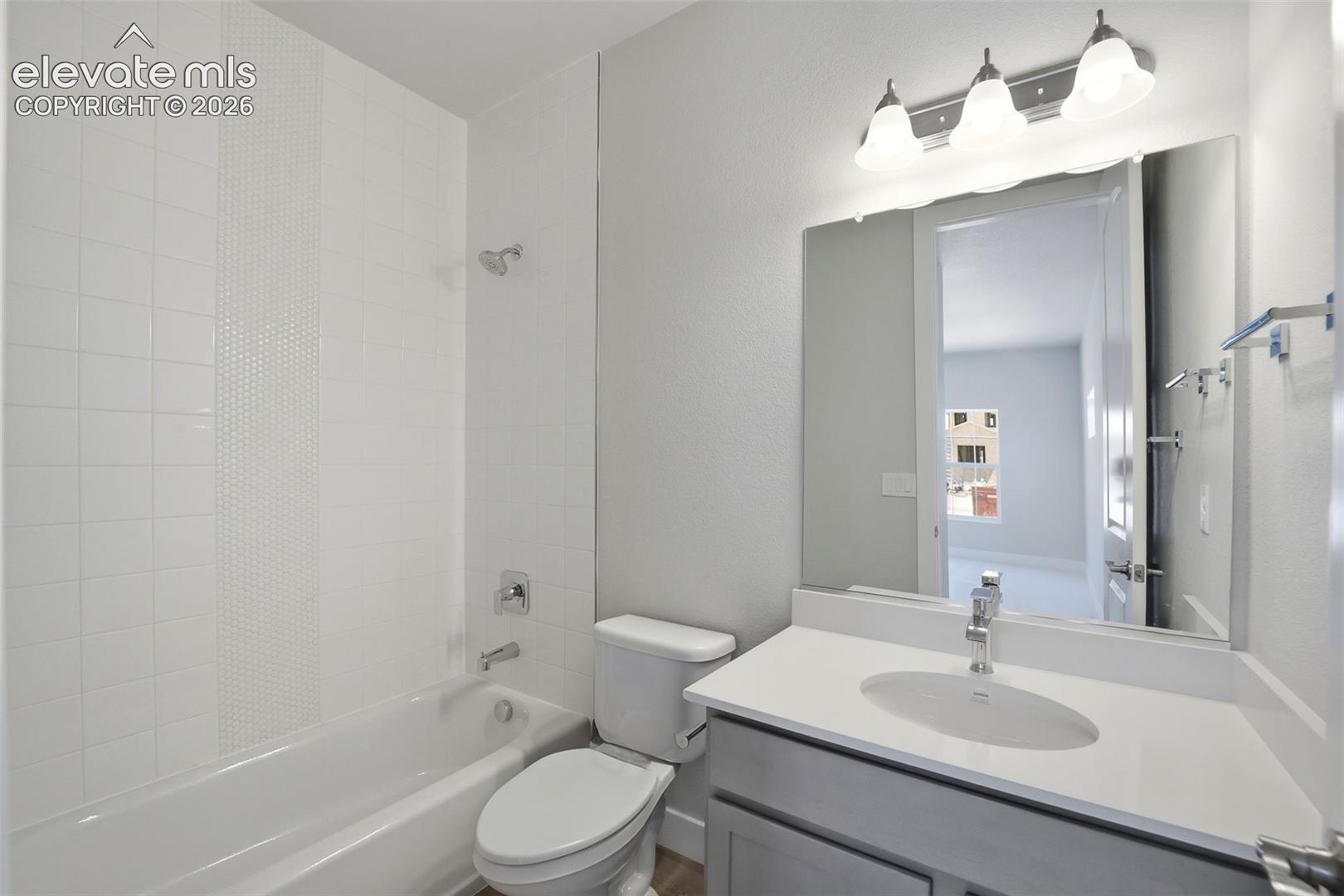 Bathroom featuring a vanity with a countertop basin, a large frameless mirror, a three-light fixture, and a tub with a tiled surround