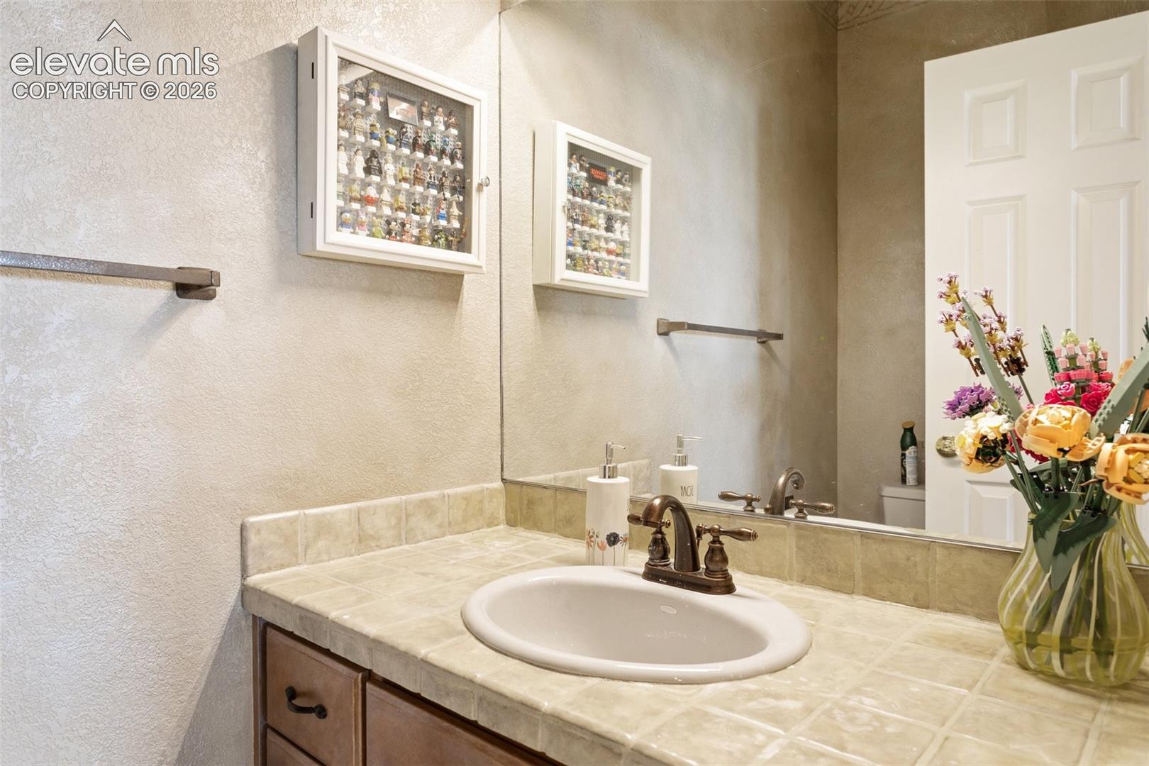Bathroom vanity featuring a tiled countertop, integrated sink, and bronze-finish faucet