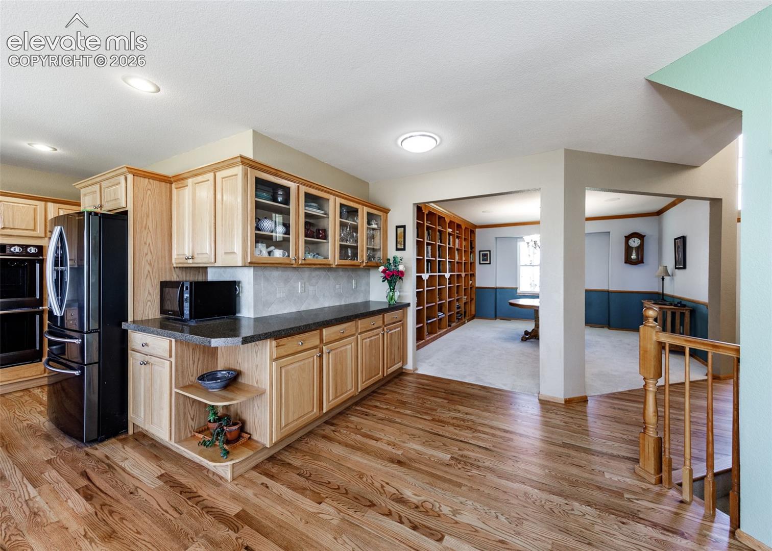 Hardwood flooring, natural wood cabinetry, built-in double oven, recessed lighting, and a built-in bookshelf wall
