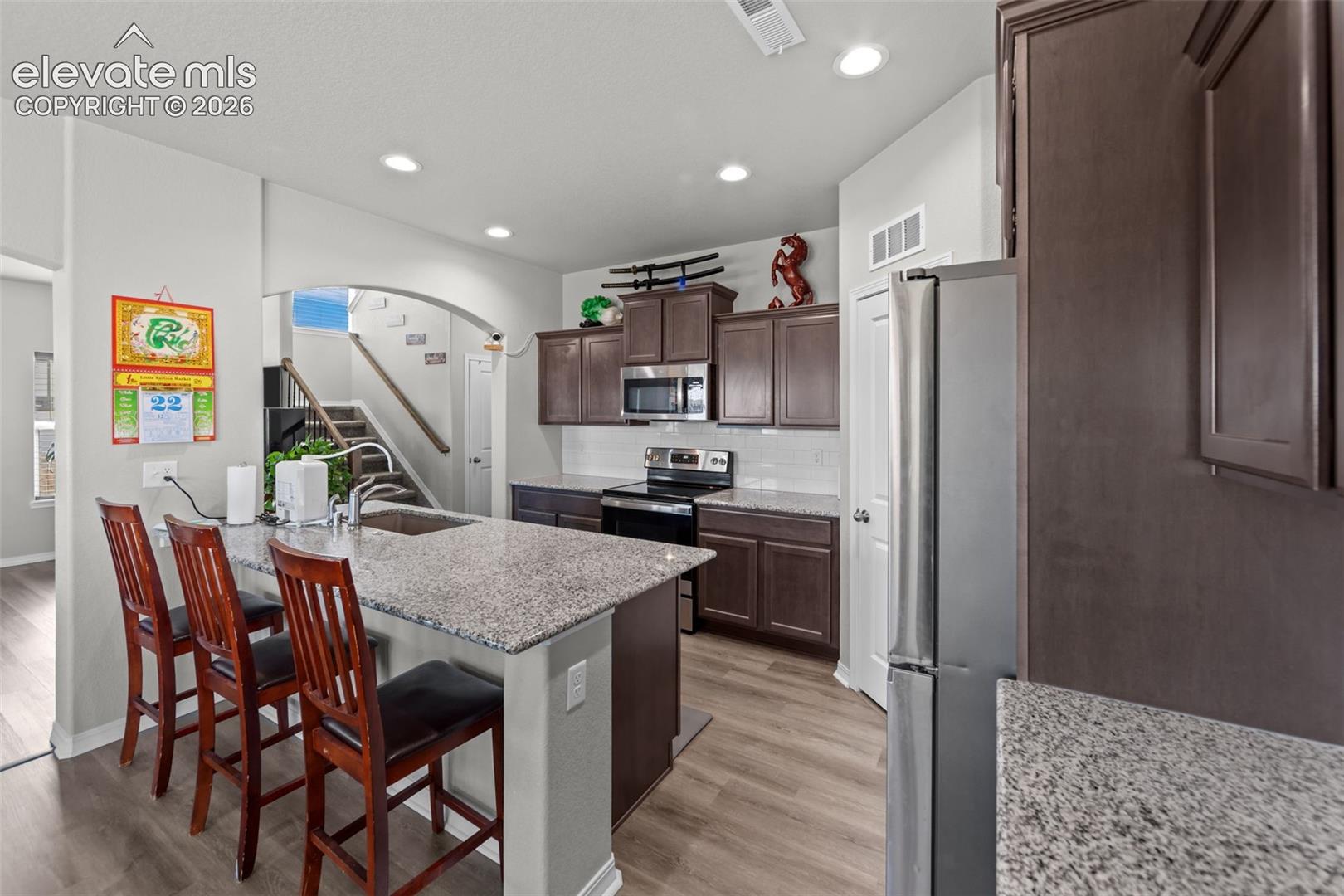 Kitchen featuring wood-finish flooring, recessed lighting, a kitchen island with seating, a stainless steel refrigerator, and dark wood cabinetry
