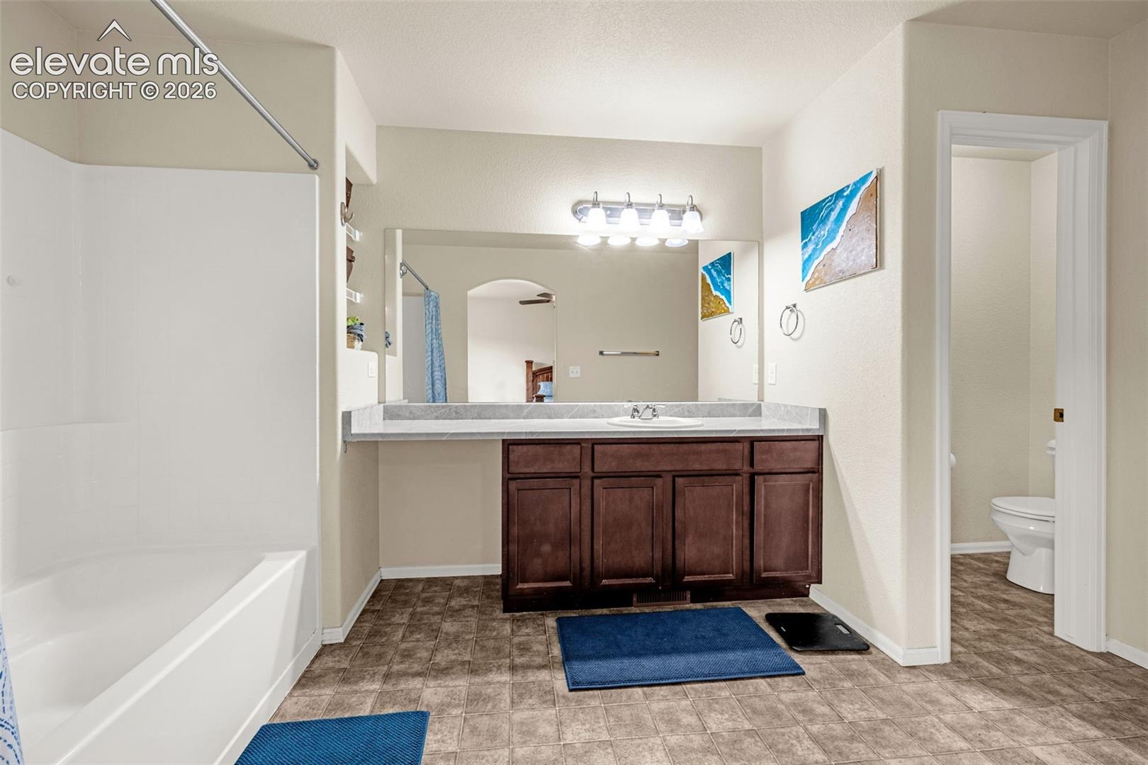 Bathroom featuring a tub/shower combination, a vanity with a single basin sink, a large mirror, and tiled flooring