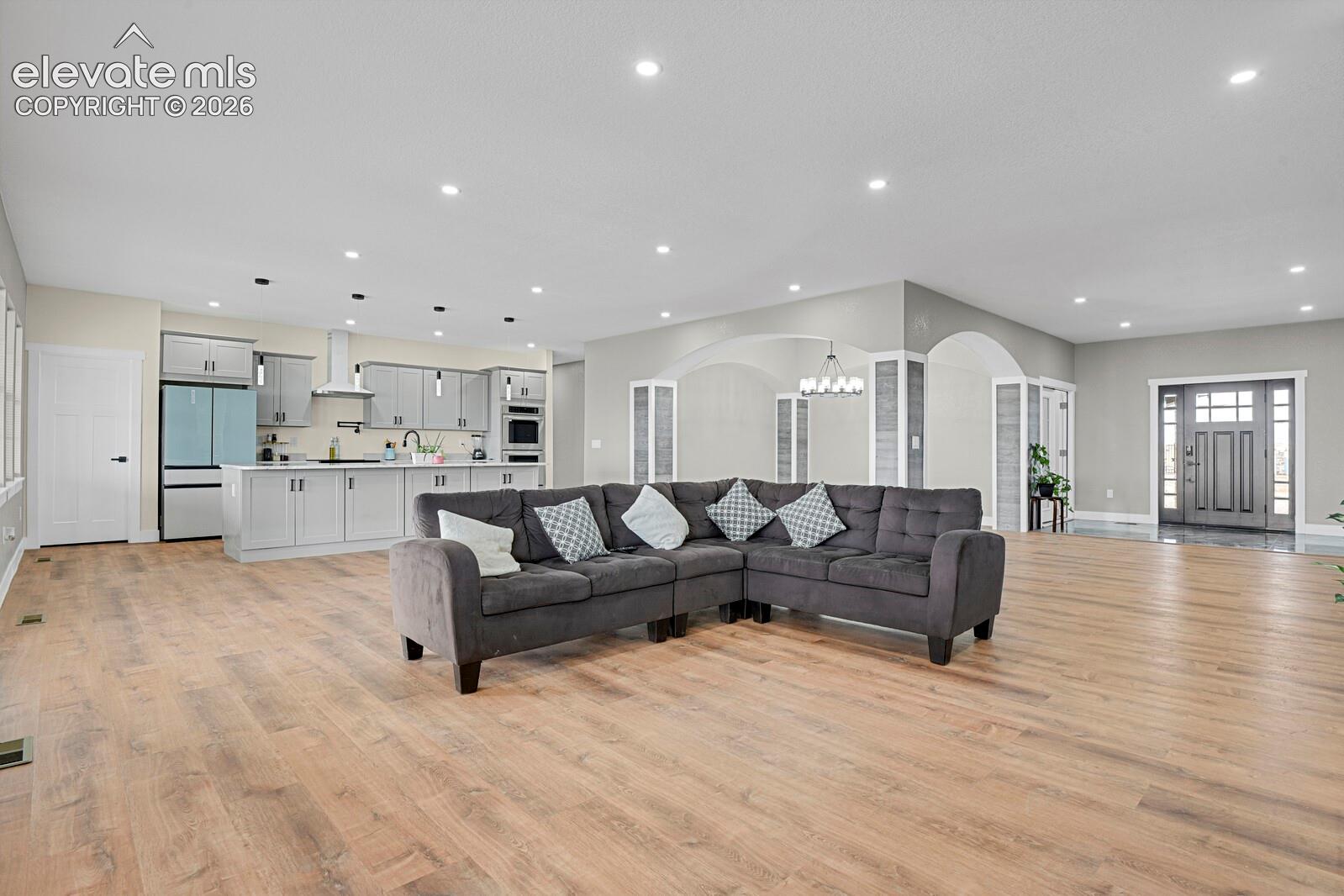 Open-concept interior featuring light wood-finish flooring, recessed lighting, arched wall detailing, and a kitchen equipped with shaker-style cabinetry and a built-in wall oven