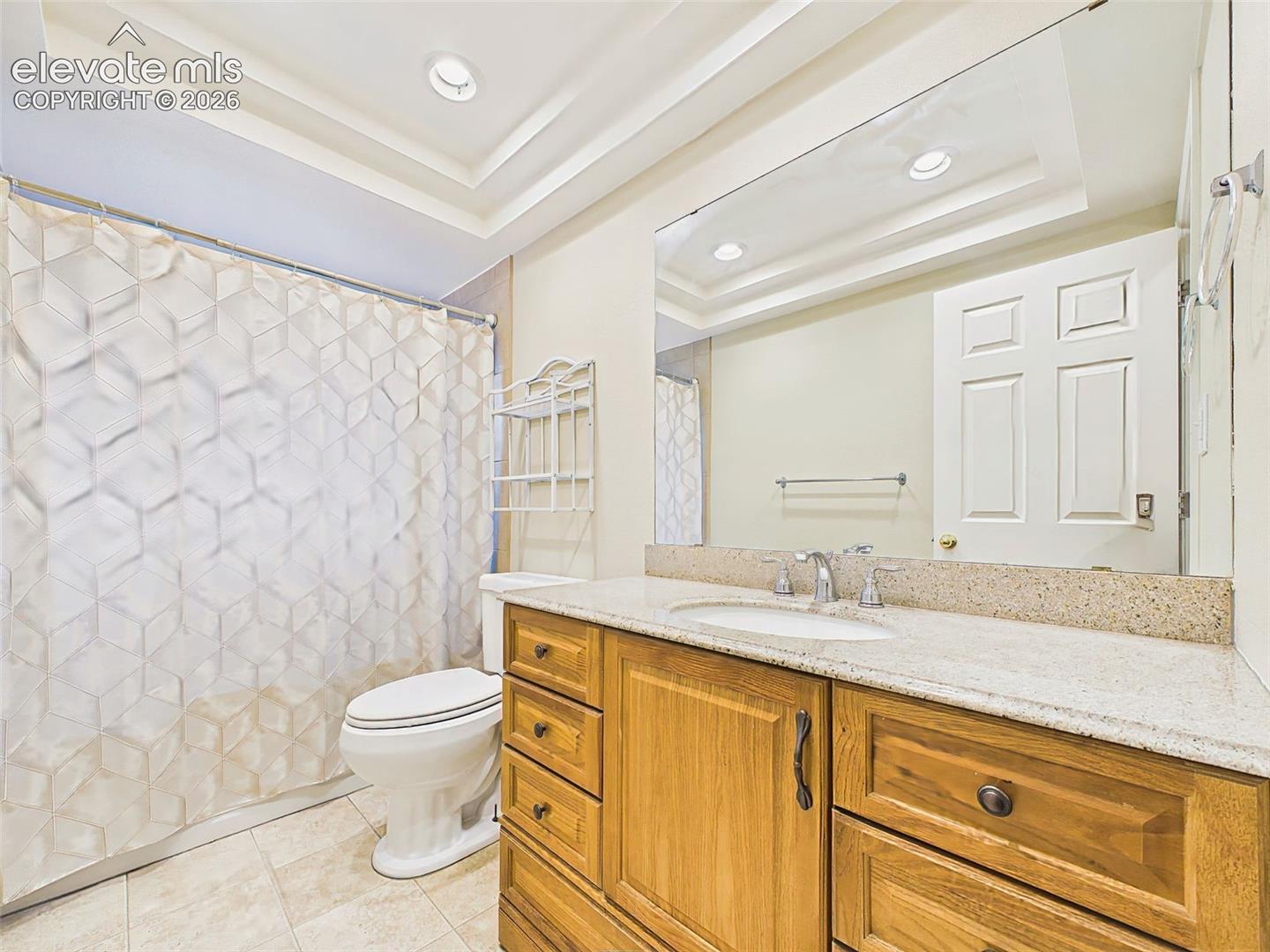 Full hall bath with a granite-topped vanity, updated lighting, and a tub/shower combination beneath a tray ceiling detail.
