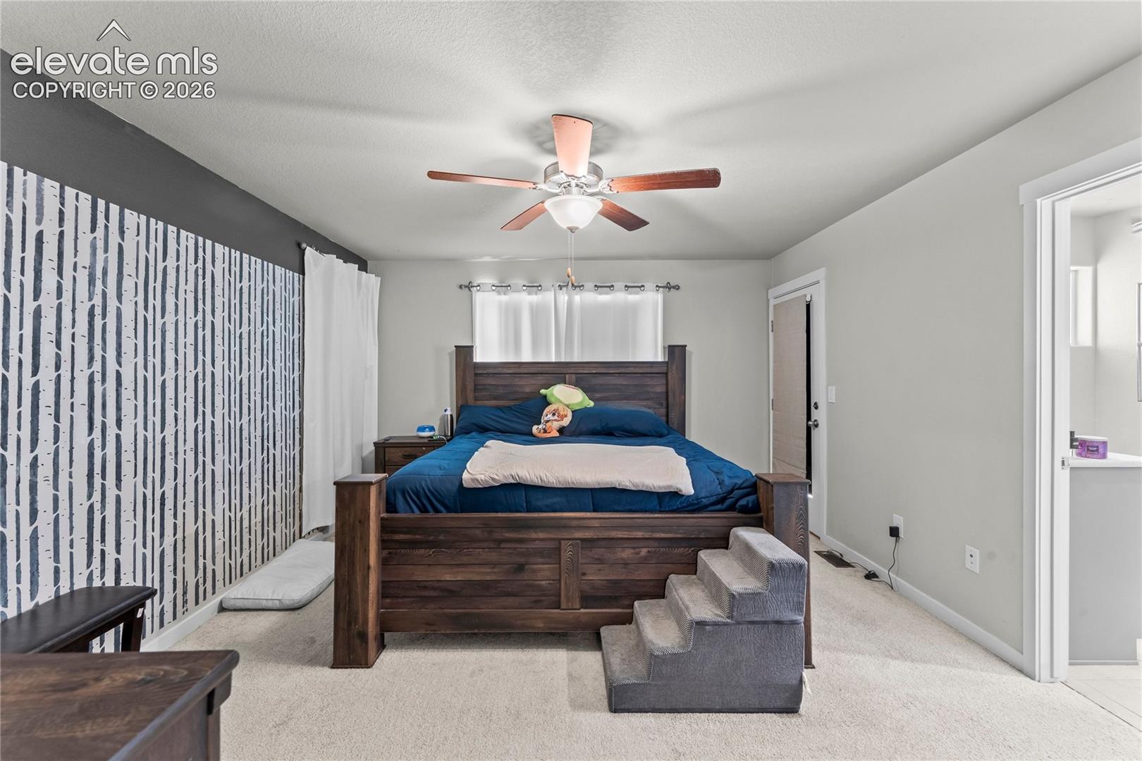 Carpeted flooring with a contrasting accent wall, ceiling fan with wood-finish blades, and a built-in light fixture