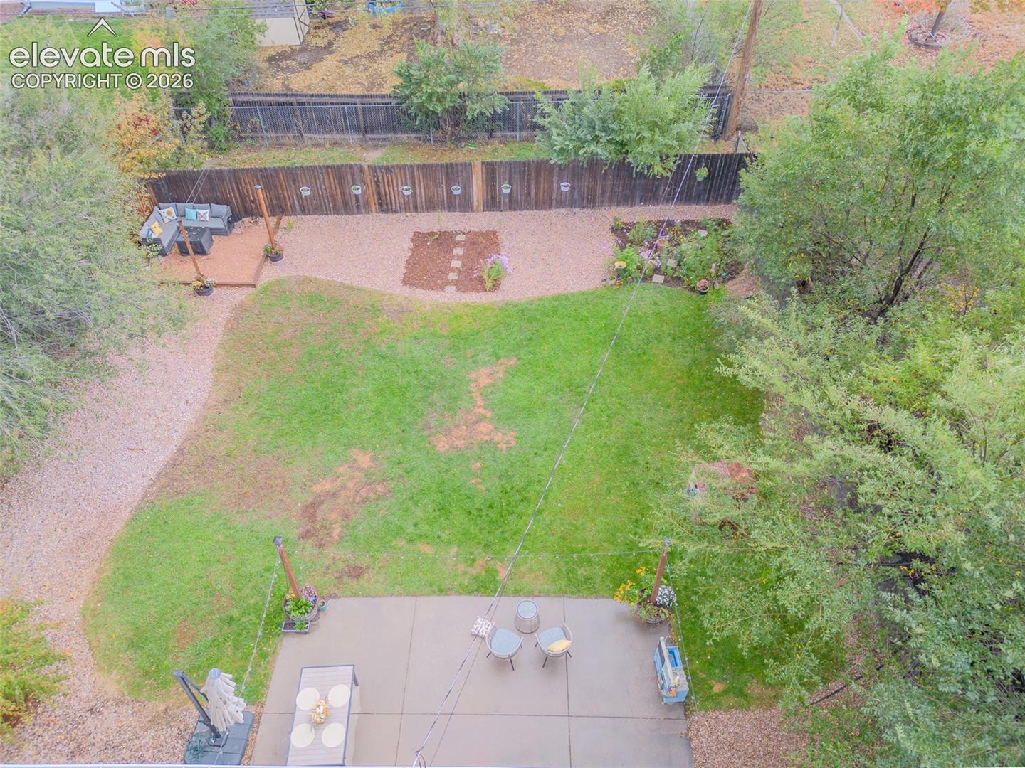 Expansive backyard featuring a concrete patio, wood deck, gravel landscaping, perimeter wood fencing, and mature trees