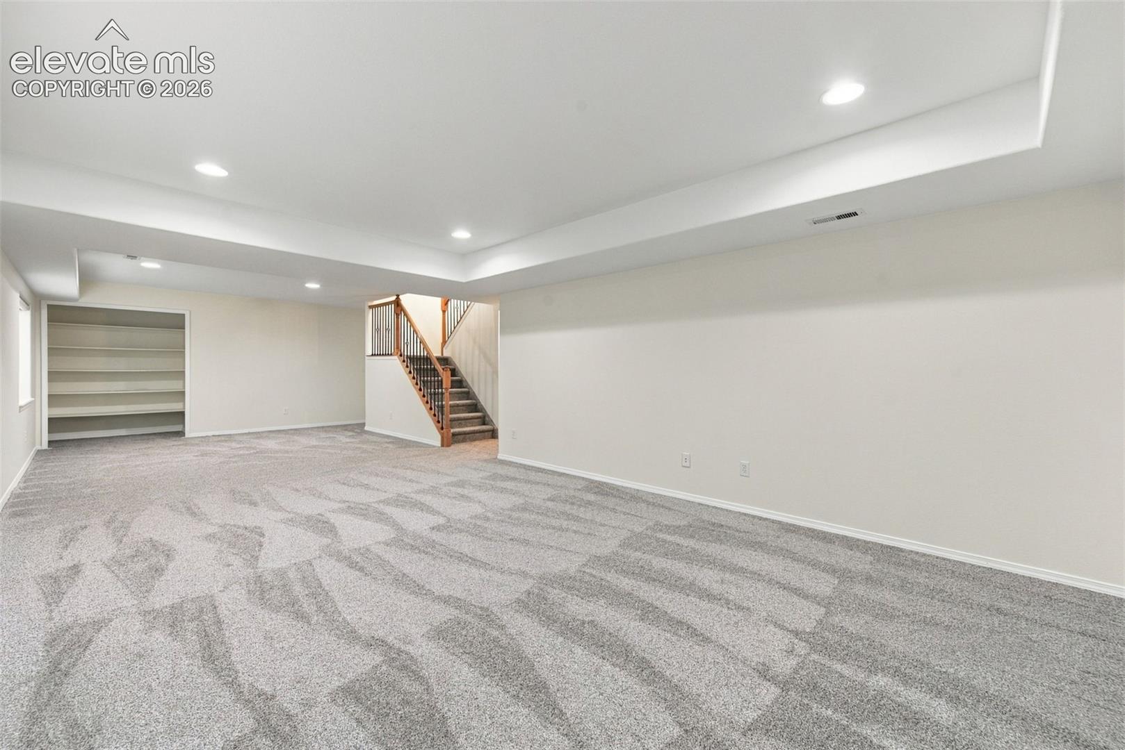 Open-concept interior featuring wall-to-wall carpeting, recessed lighting, drop-ceiling detailing, built-in shelving, and a staircase with wood-finish handrails